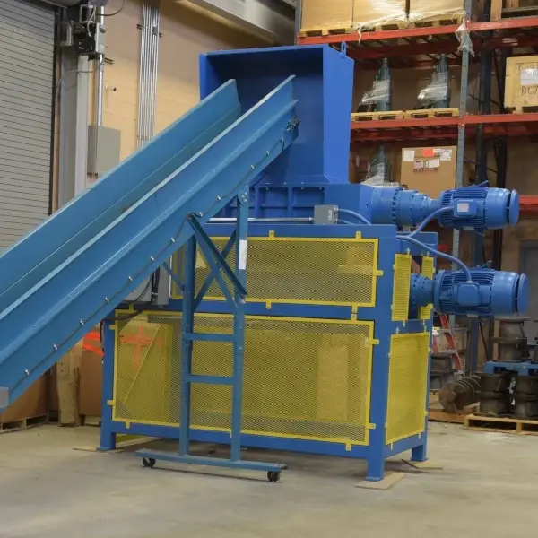 An industrial shredder with a conveyor sitting on the floor of a warehouse