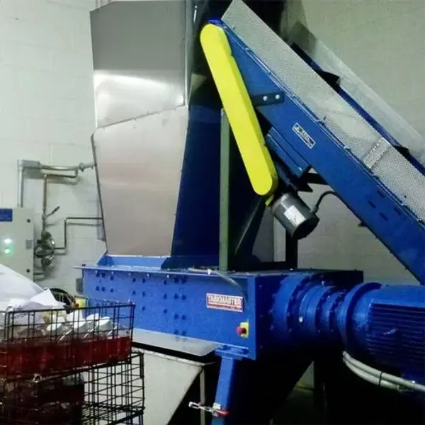 A large industrial shredder with a conveyor attachment in a warehouse