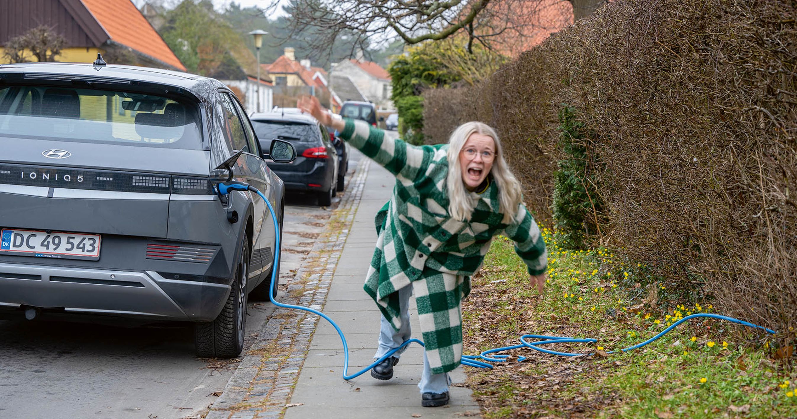 Kvinde er ved at snuble over ladekabel, der ligger henover fortov.