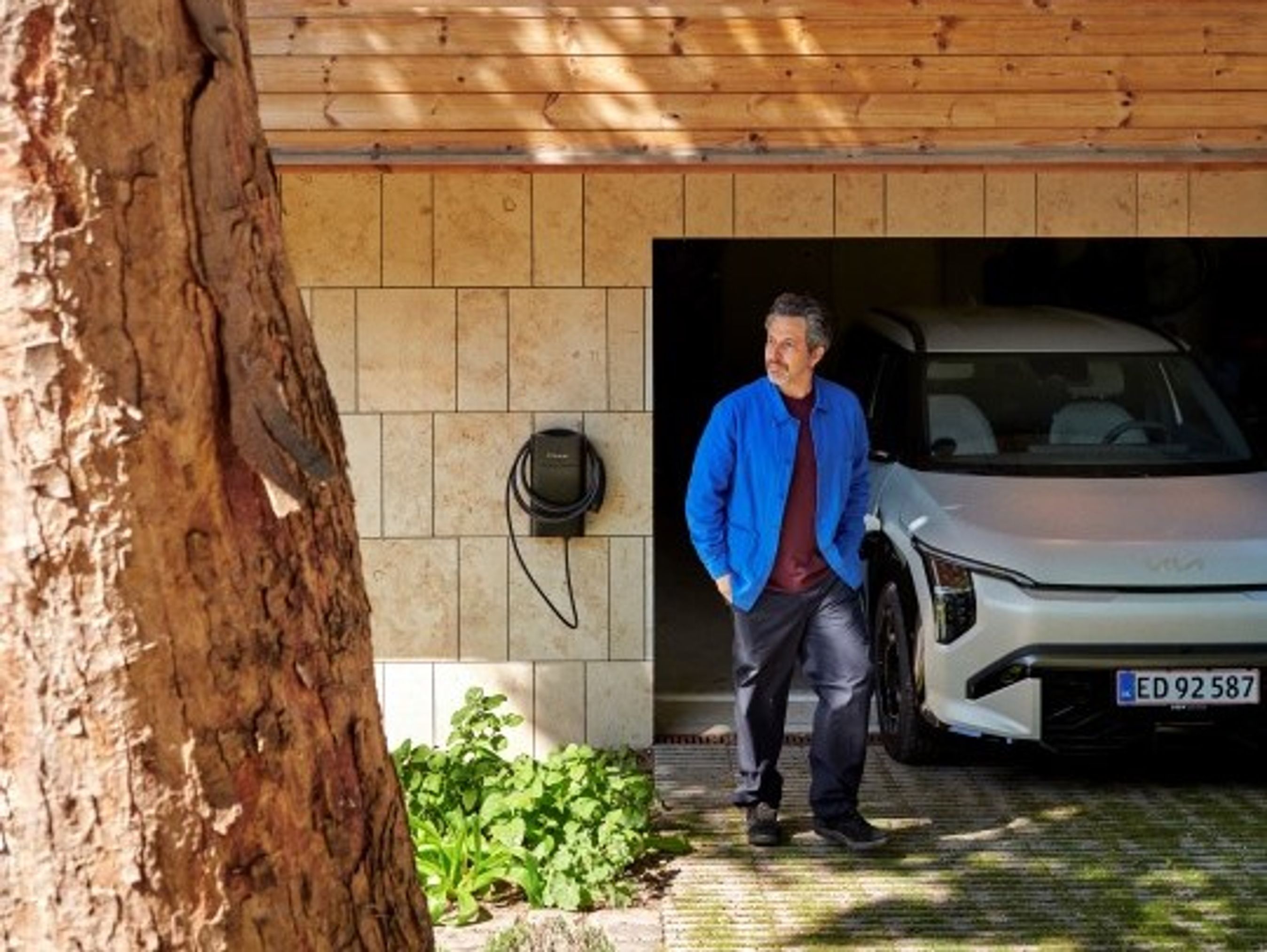 Mand kommer ud af garage med hvid elbil og clever ladeboks