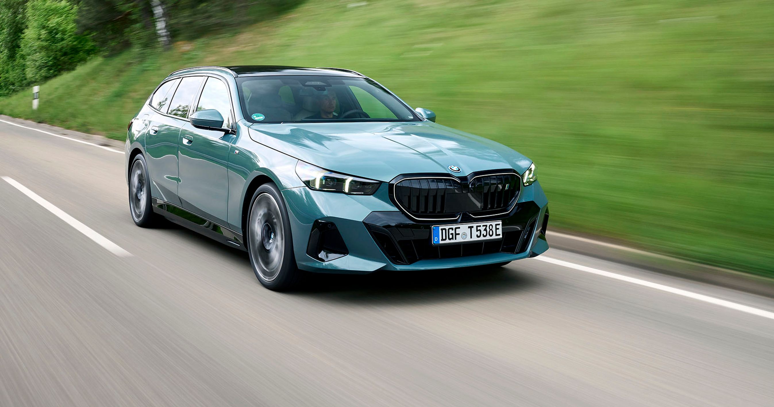 Grøn BMW i5 Touring kører på en vej med græs i baggrunden