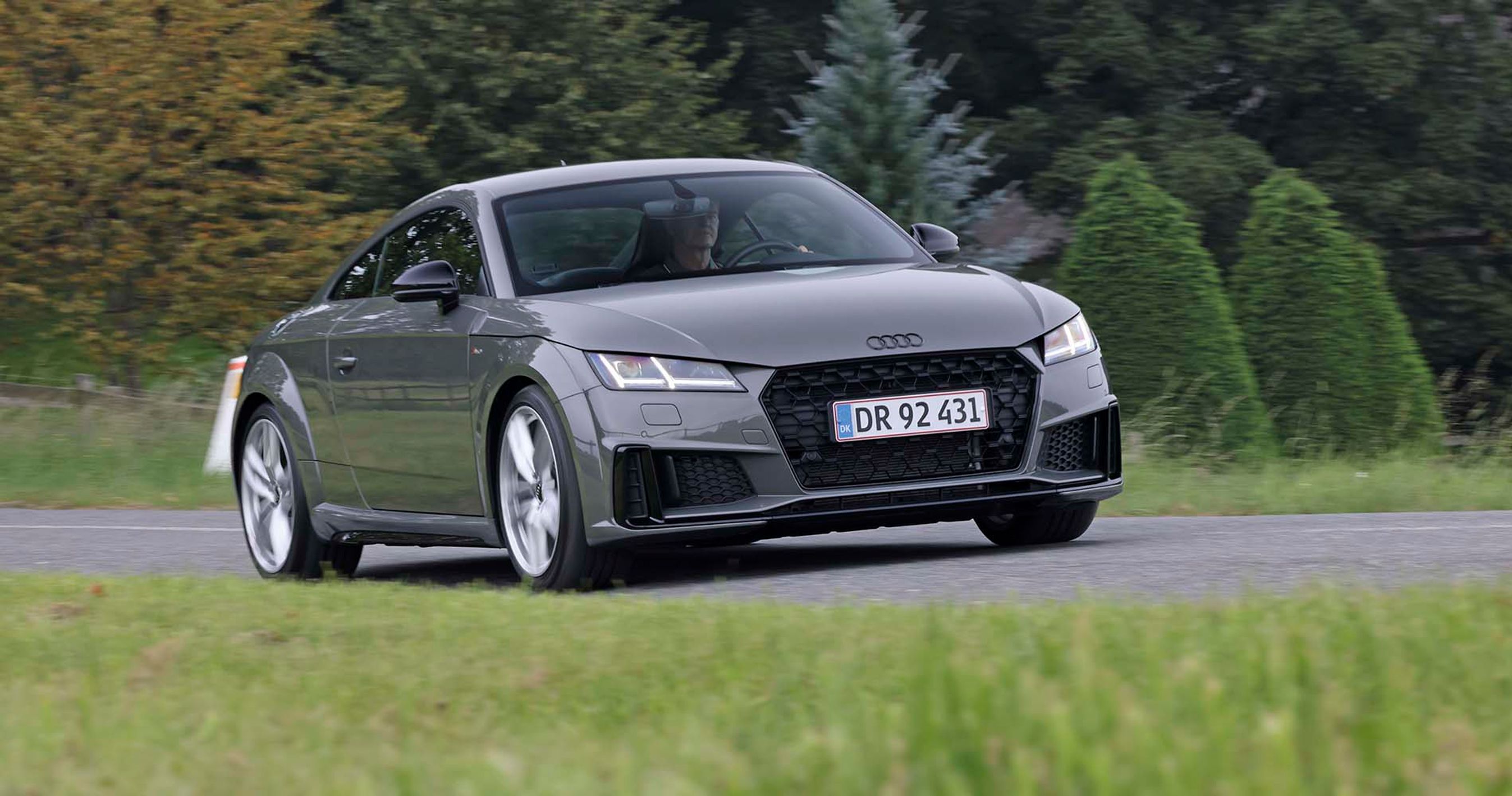 En Audi TT kører på en landevej med græs i forgrunden og træer i baggrunden