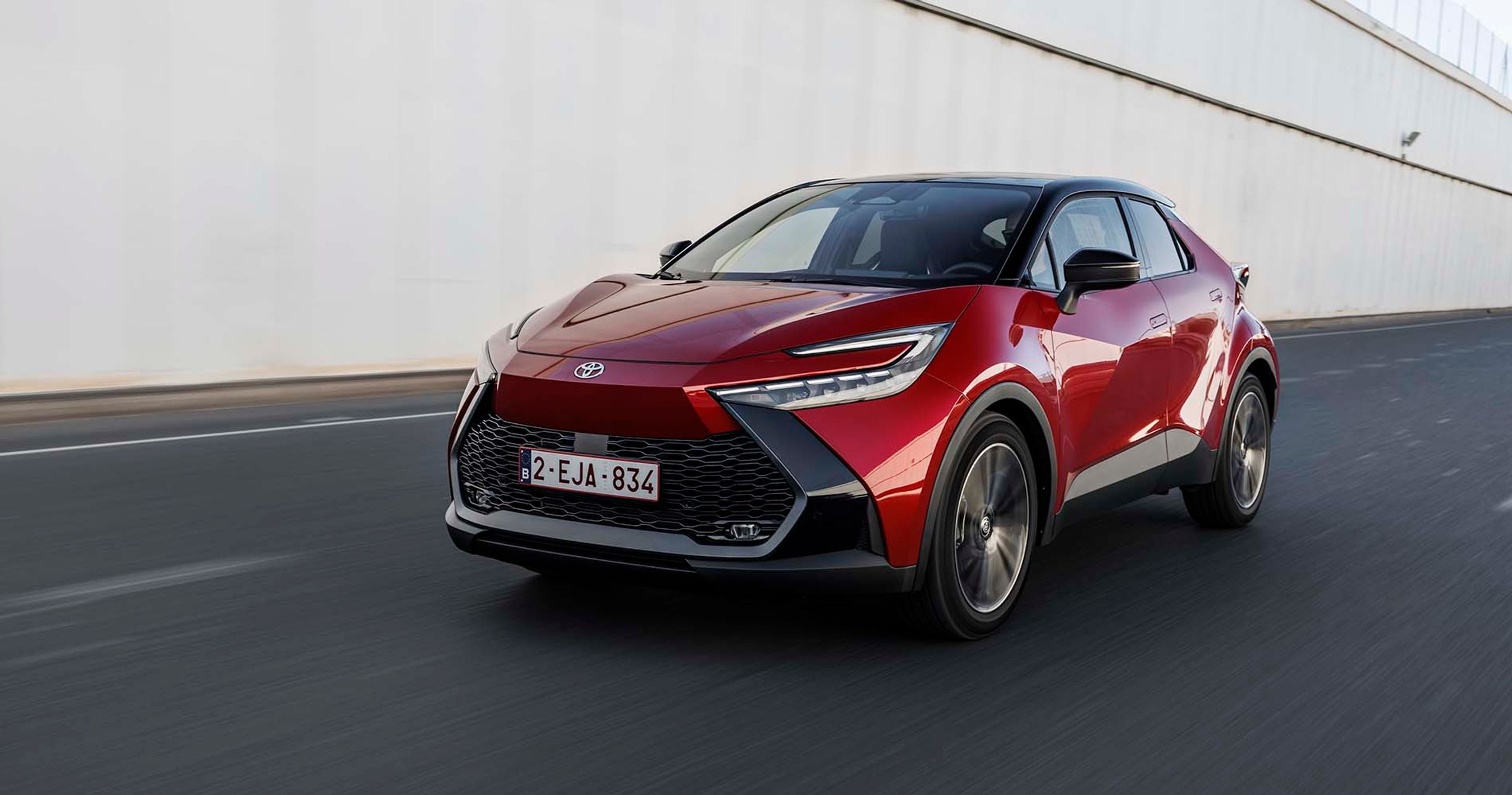 En rød Toyota C-HR kører på en motorvej med støjværn i baggrunden