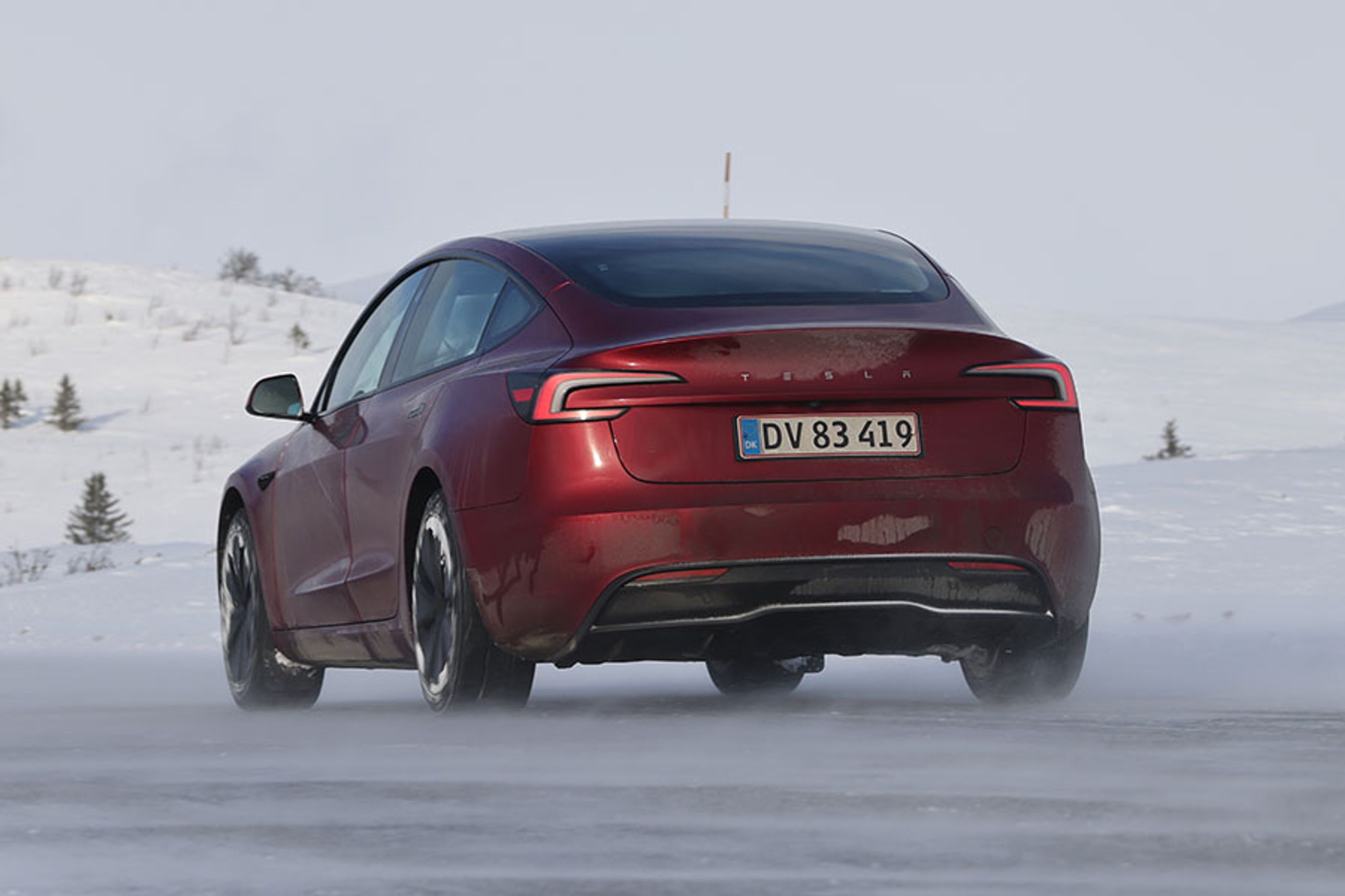Rød Tesla Model 3 set bagfra kører i snelandskab