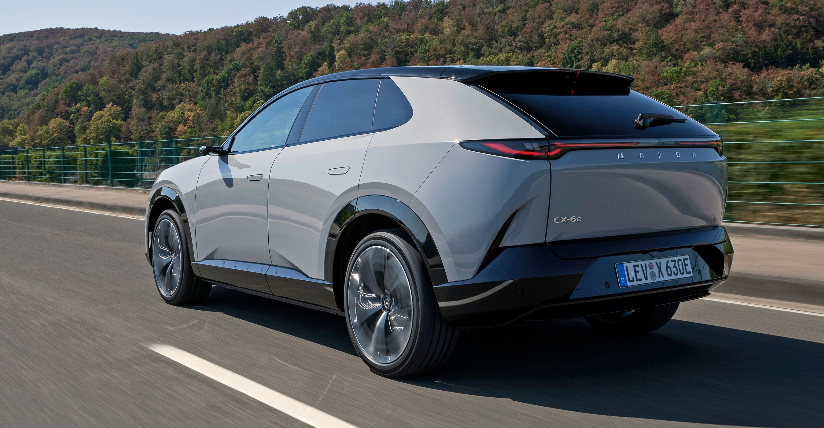 Lys Mazda CX-6e kørende på landevej set bagfra.