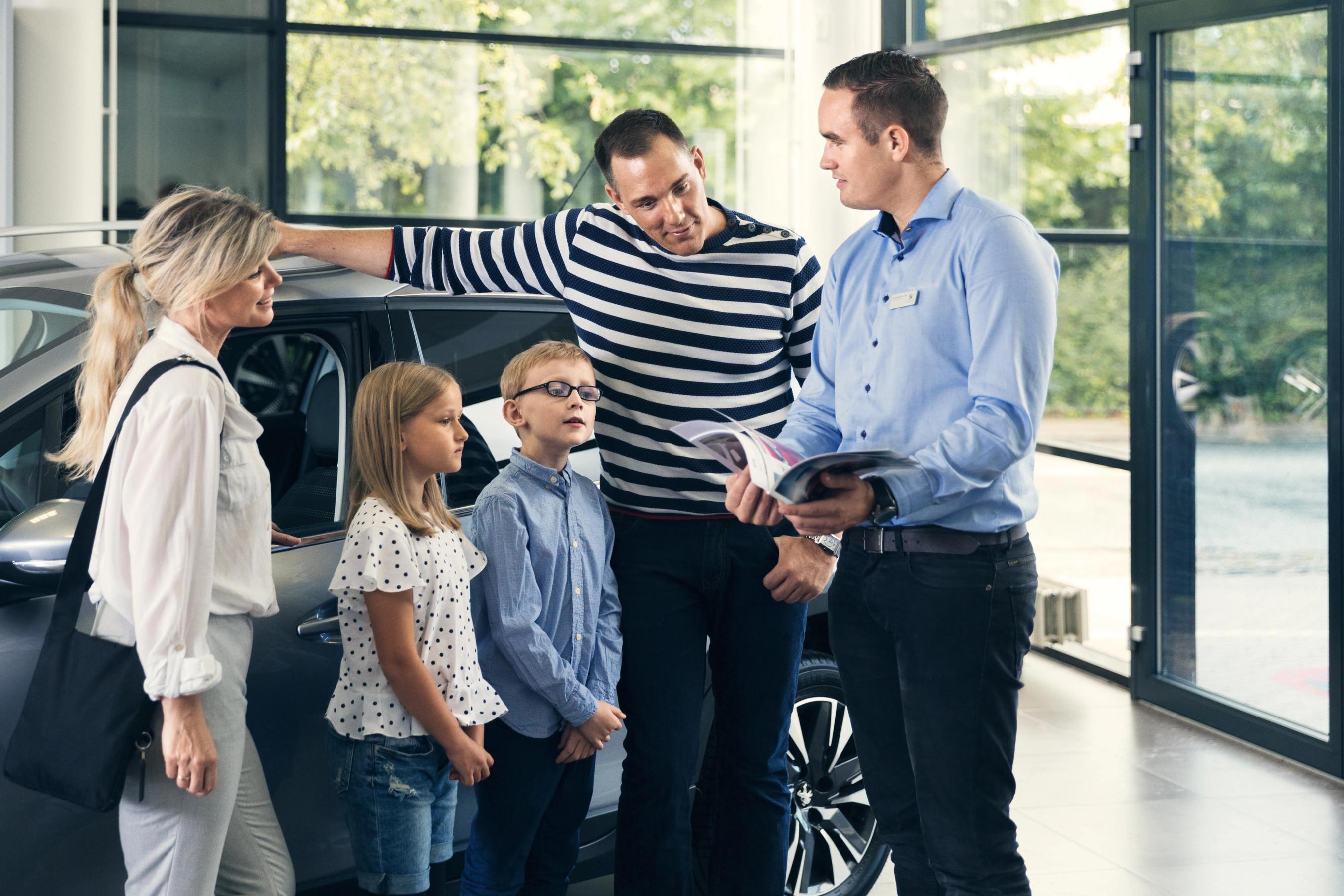 Familie i butik, som sælger biler. Bilsælger viser et katalog frem for familien.