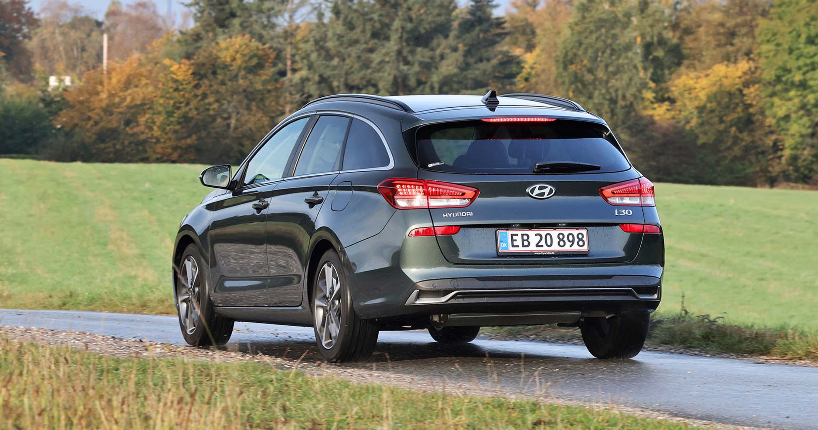 En sort Hyundai i30 stationcar set bagfra, mens den kører på en landevej med græs i baggrunden