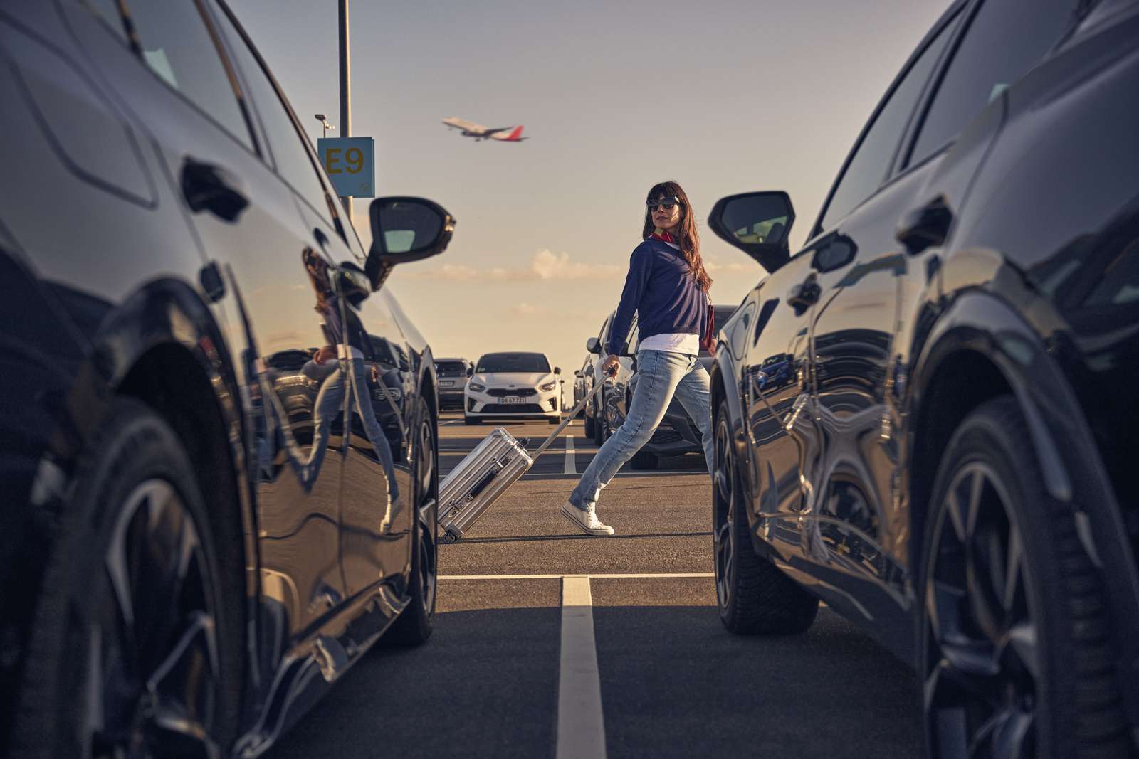Kvinde med kuffert på en parkeringsplads