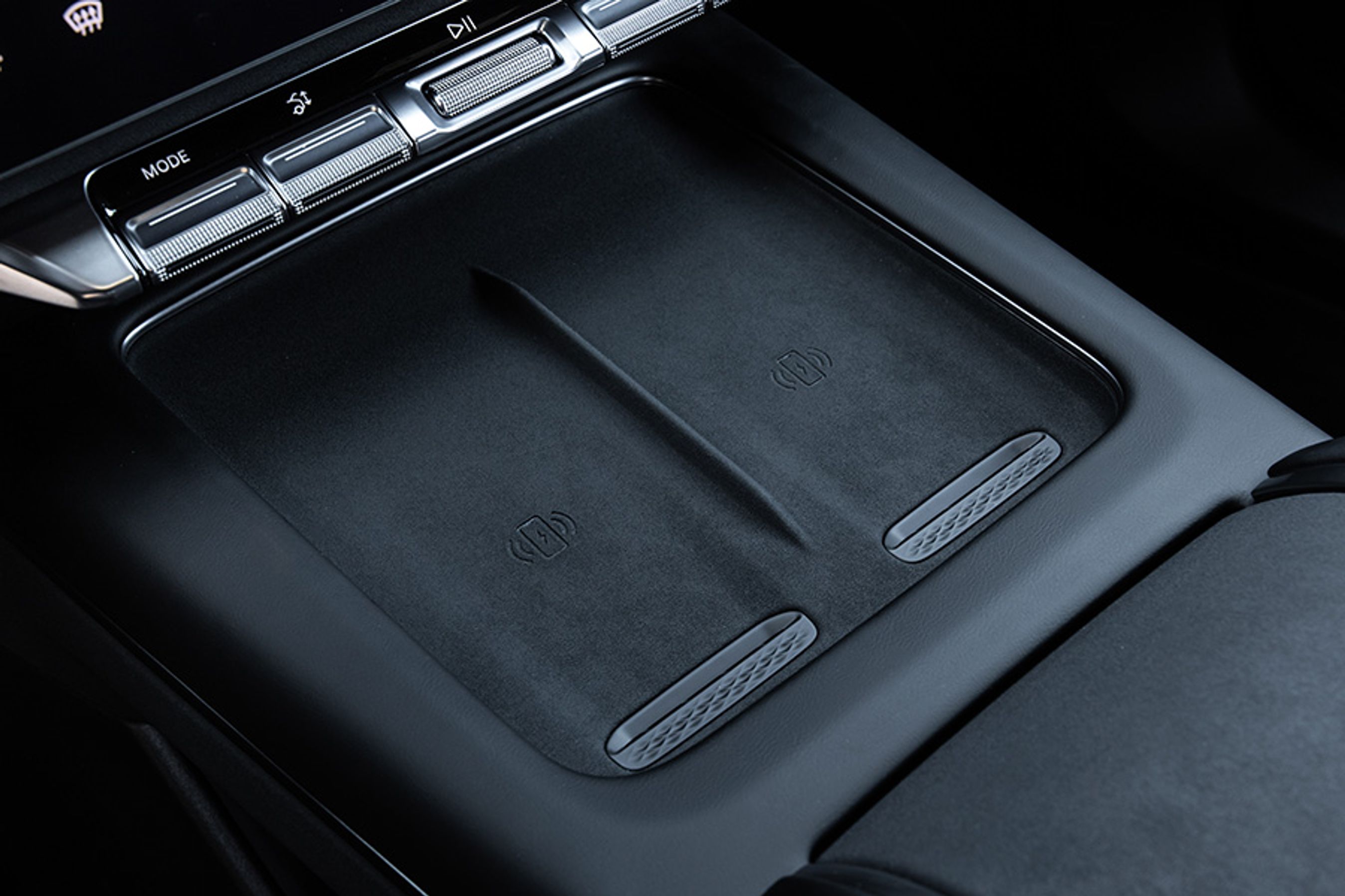 Der er to pladser til trådløs opladning af mobiltelefoner. De lader hver med 50 Watt og er luftkølet. I midten ovenfor ses drejeknappen til lydsystemets volumen.