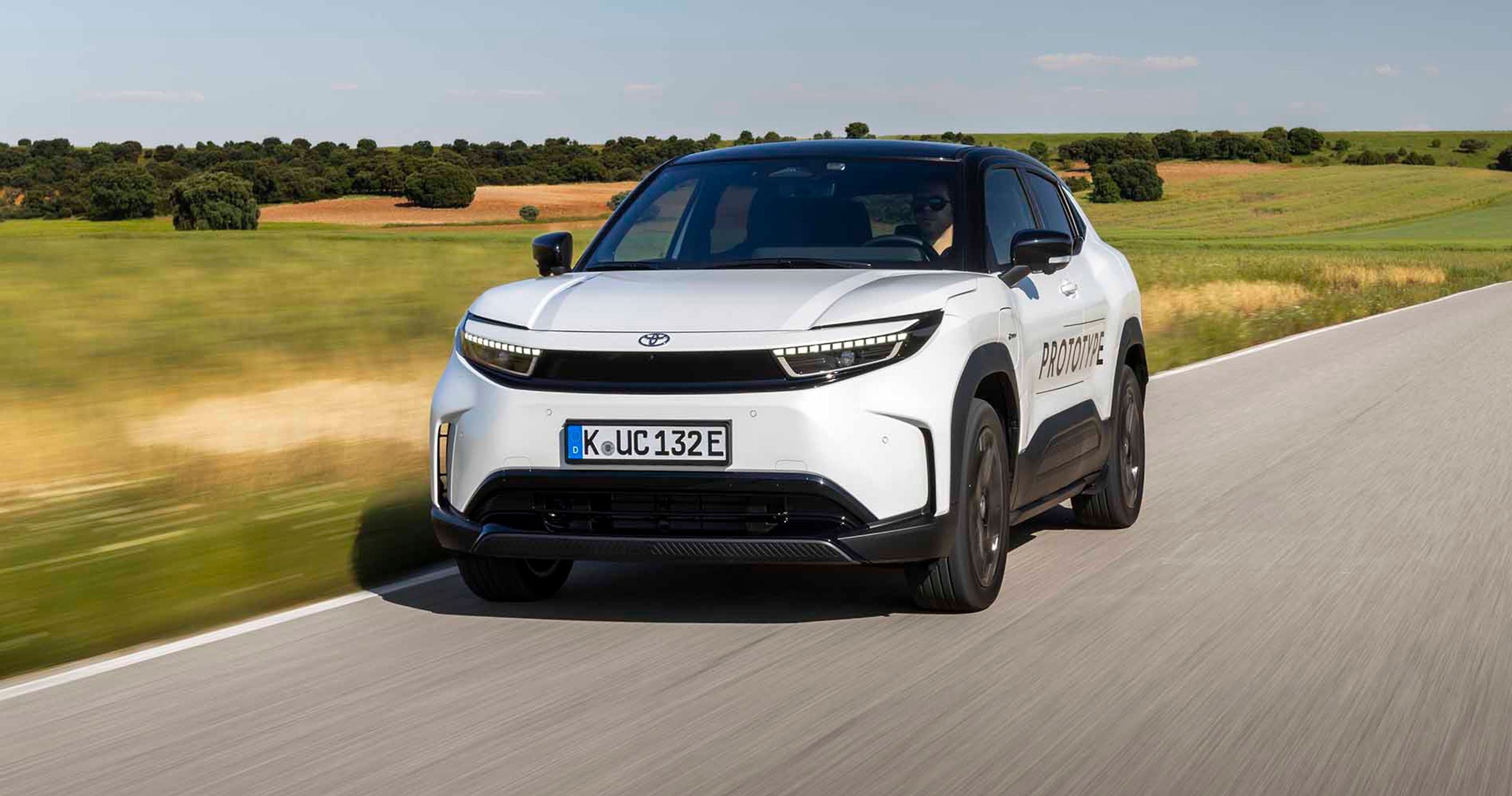 Hvid Toyota Urban Cruiser kører på vej med marker i baggrunden