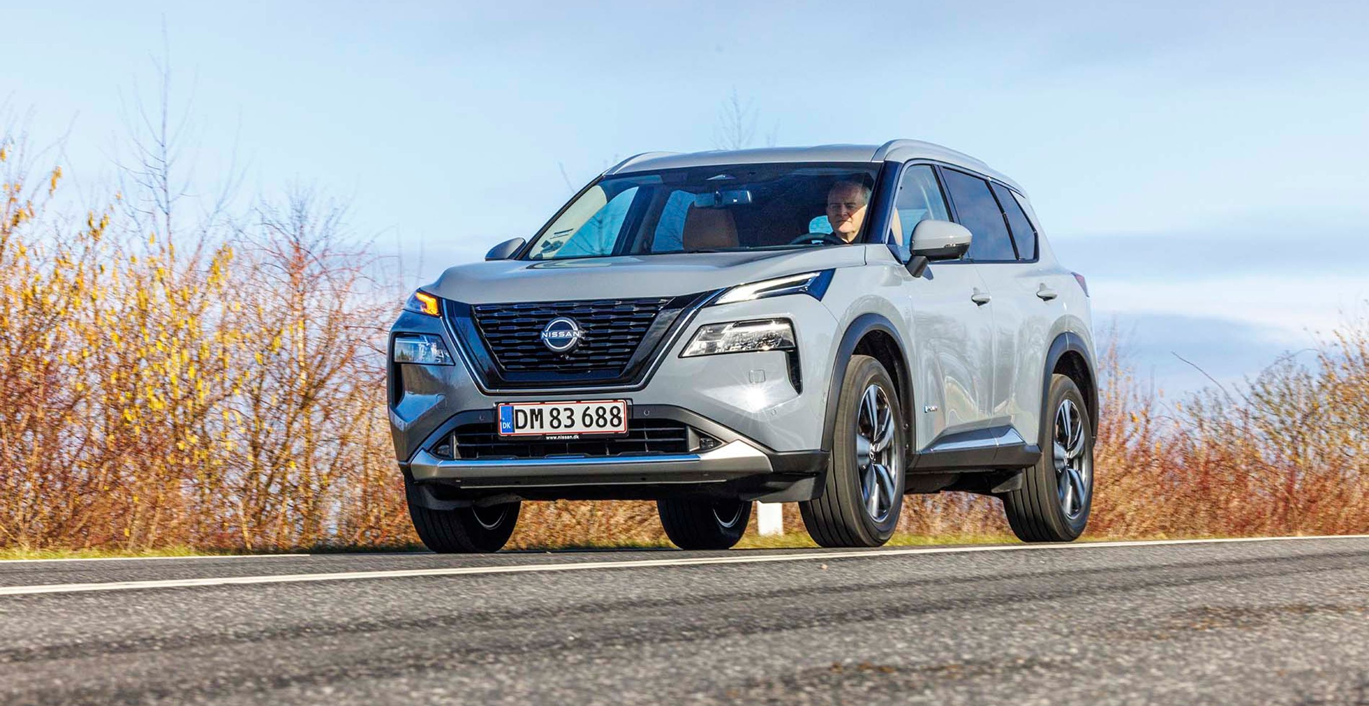 Nissan X-Trail kører på en vej med buskads i baggrunden