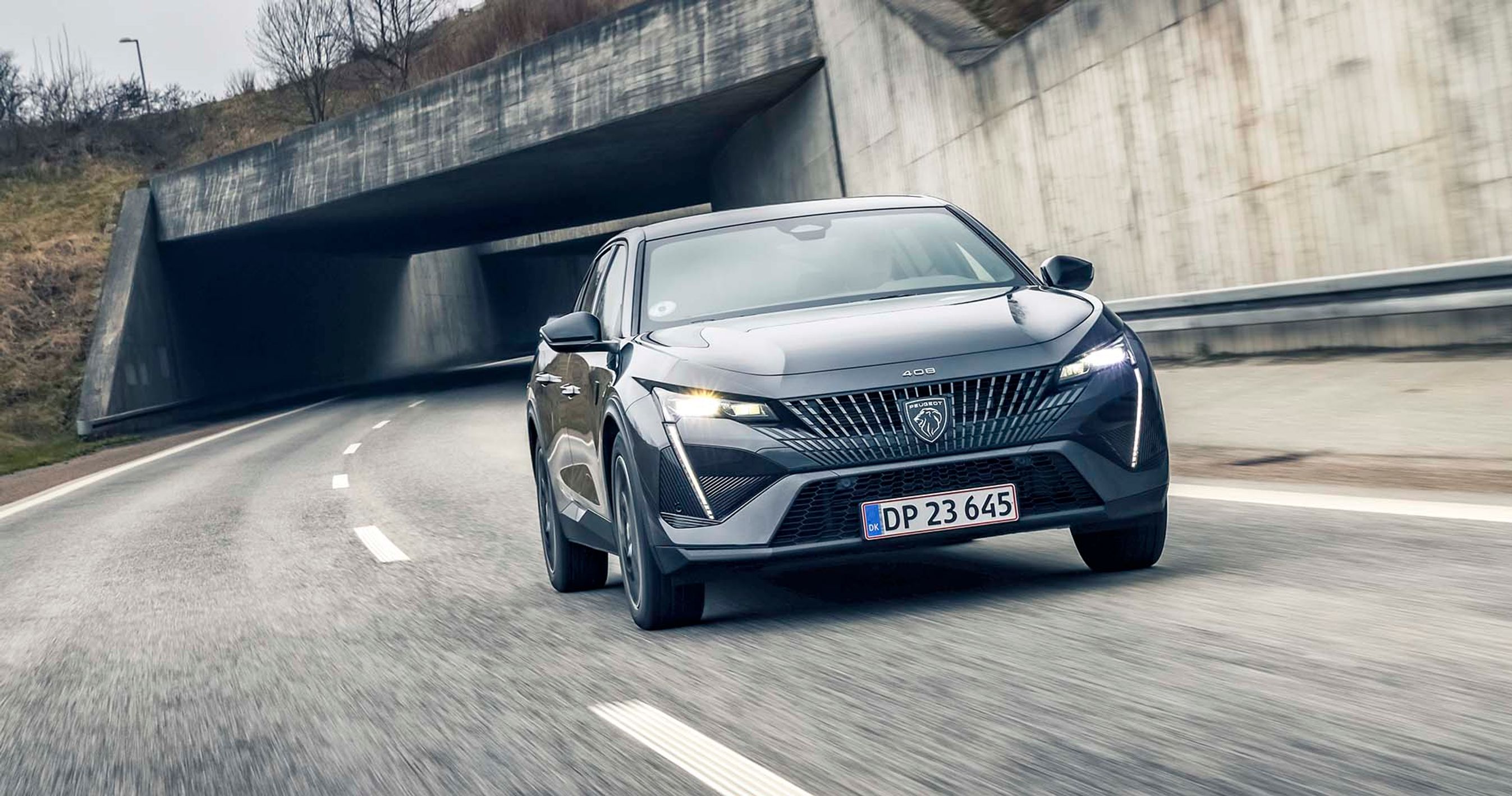 En sort Peugeot 408 kører på en motorvej med en betonbro i baggrunden