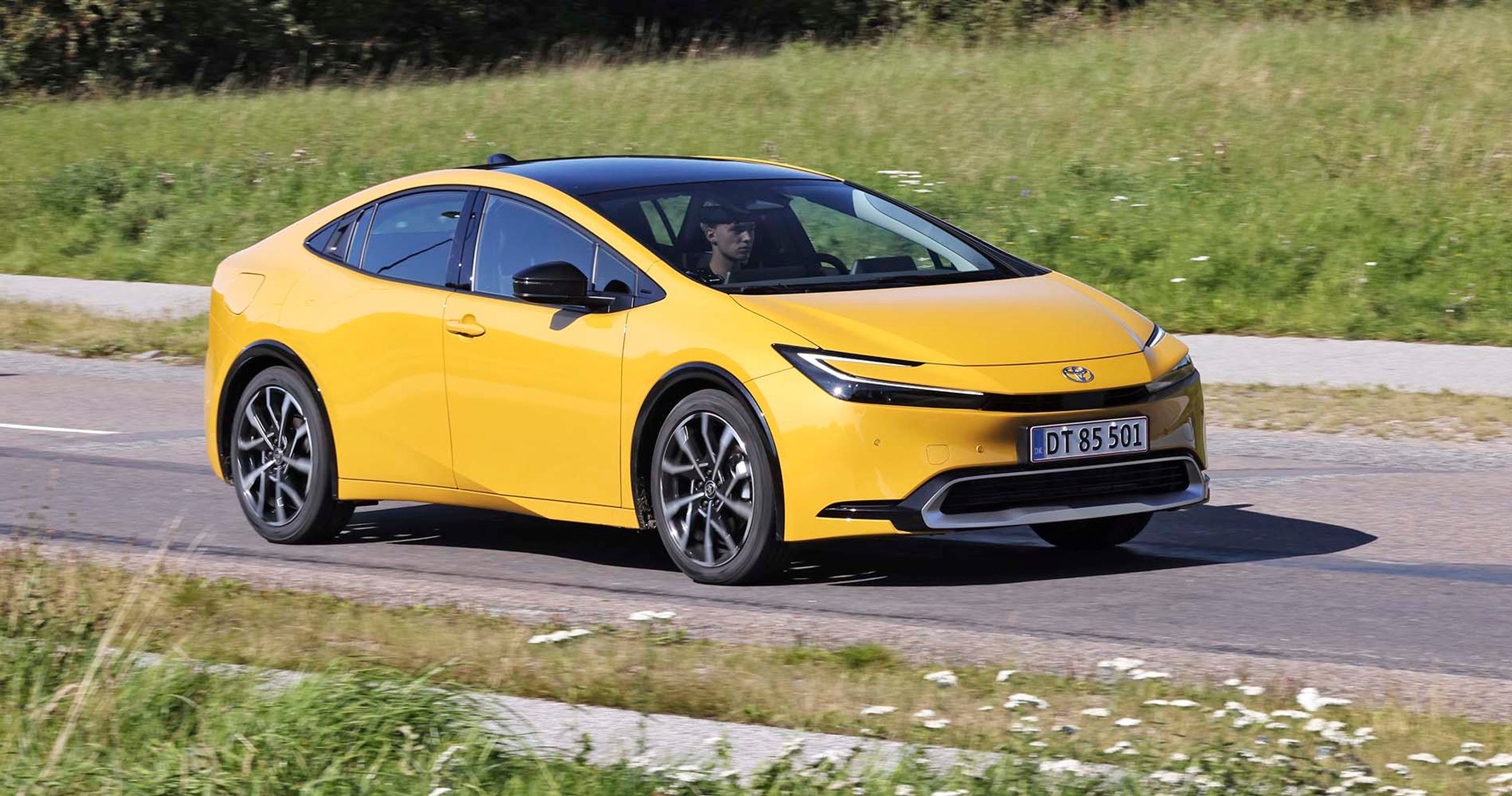 En gul Toyota Prius kører på en alndevej med græs på begge sider.