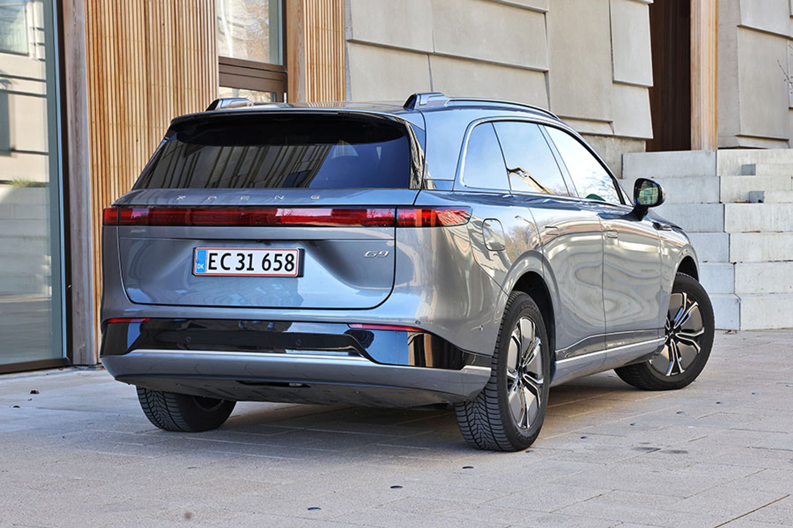 Xpeng G9 set bagfra, mens den er parkeret foran bygning med træpaneler på facaden