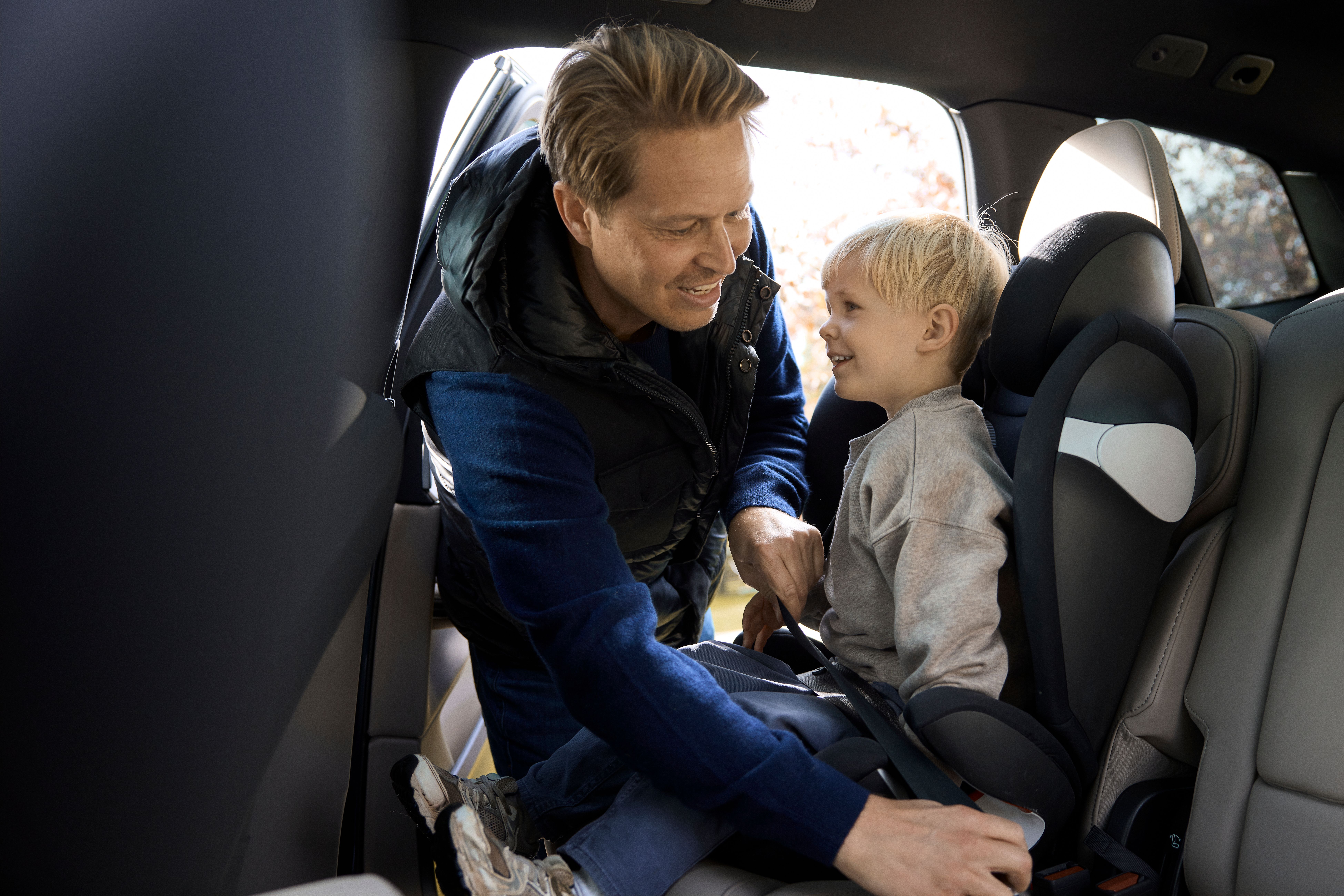 Mand placerer barn i autostol og spænder sikkerhedsselen