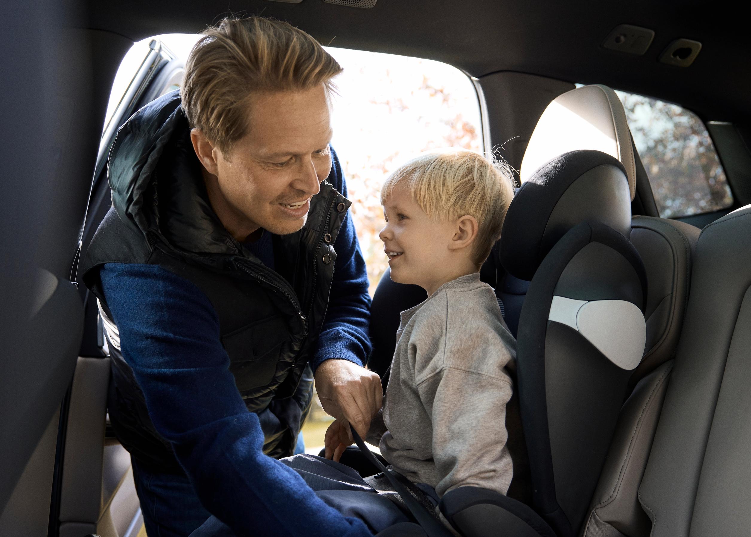 Mand placerer barn i autostol og spænder sikkerhedsselen