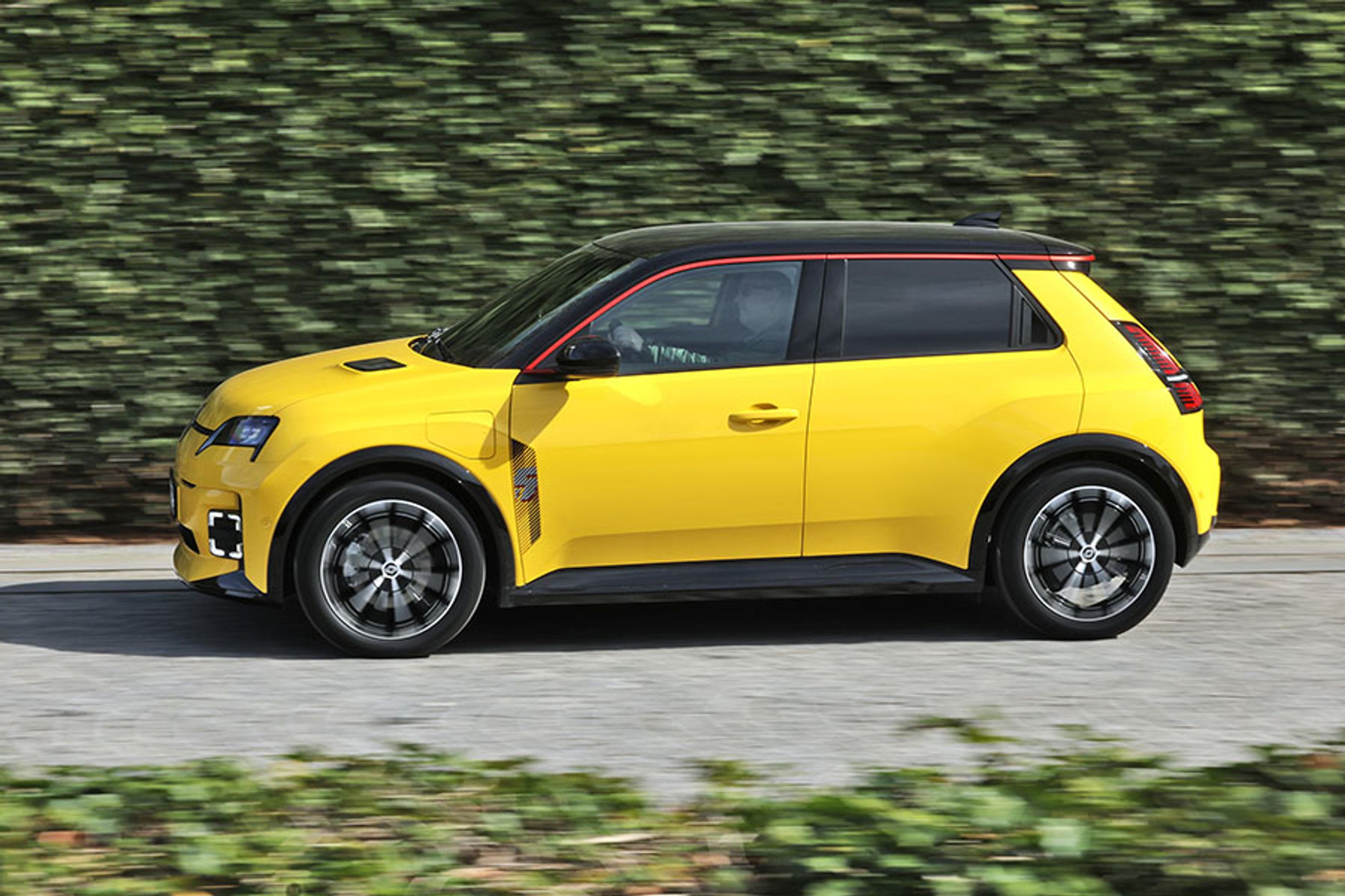 Gul Renault 5 set fra siden, mens den kører foran en hæk