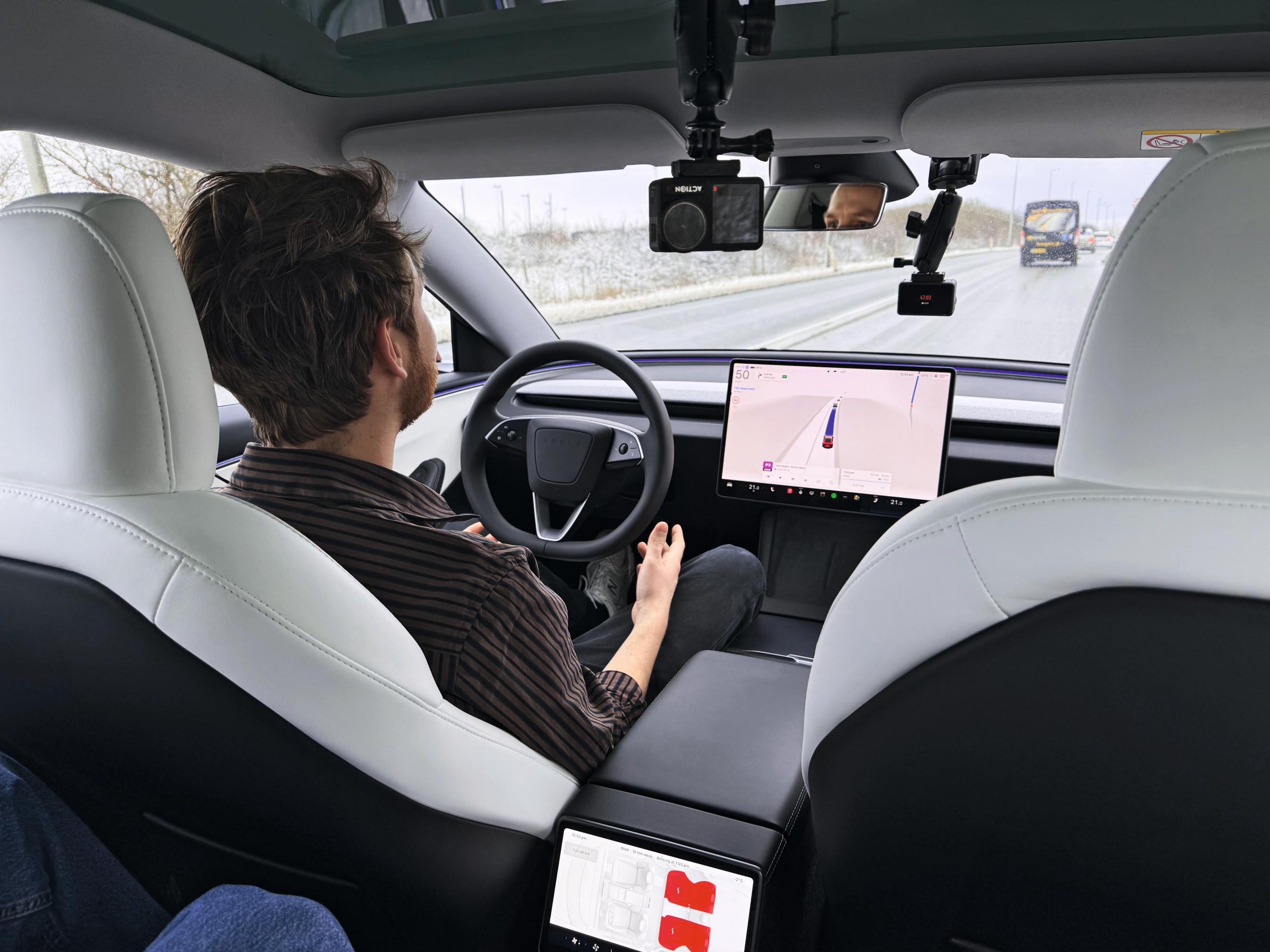 Mand sidder bag rattet i en Tesla med selvkørende teknik. Derfor holder han ikke om rattet