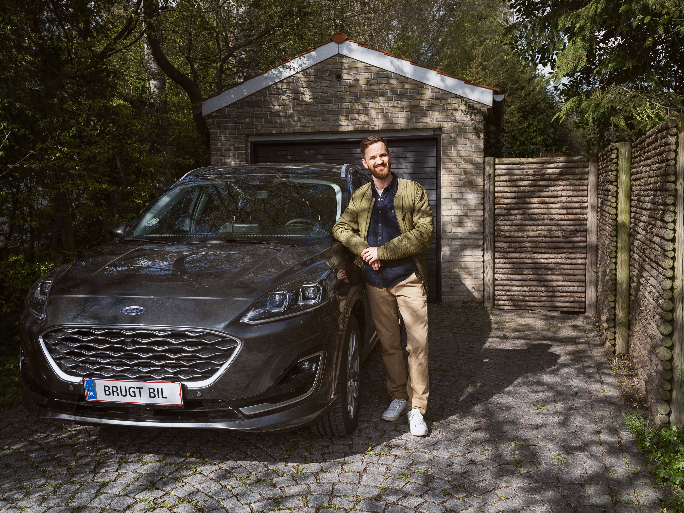 Mand står ved siden af sin brugte bil, som holder i en carport