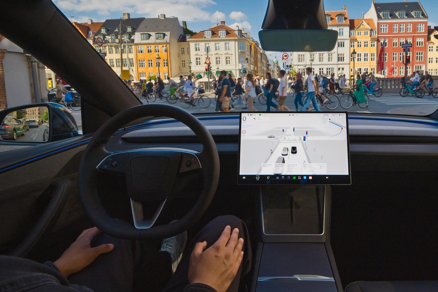 Førerpladsen i en Tesla, hvor føreren ikke har hænderne på rattet. Nyhavn i baggrunden. 