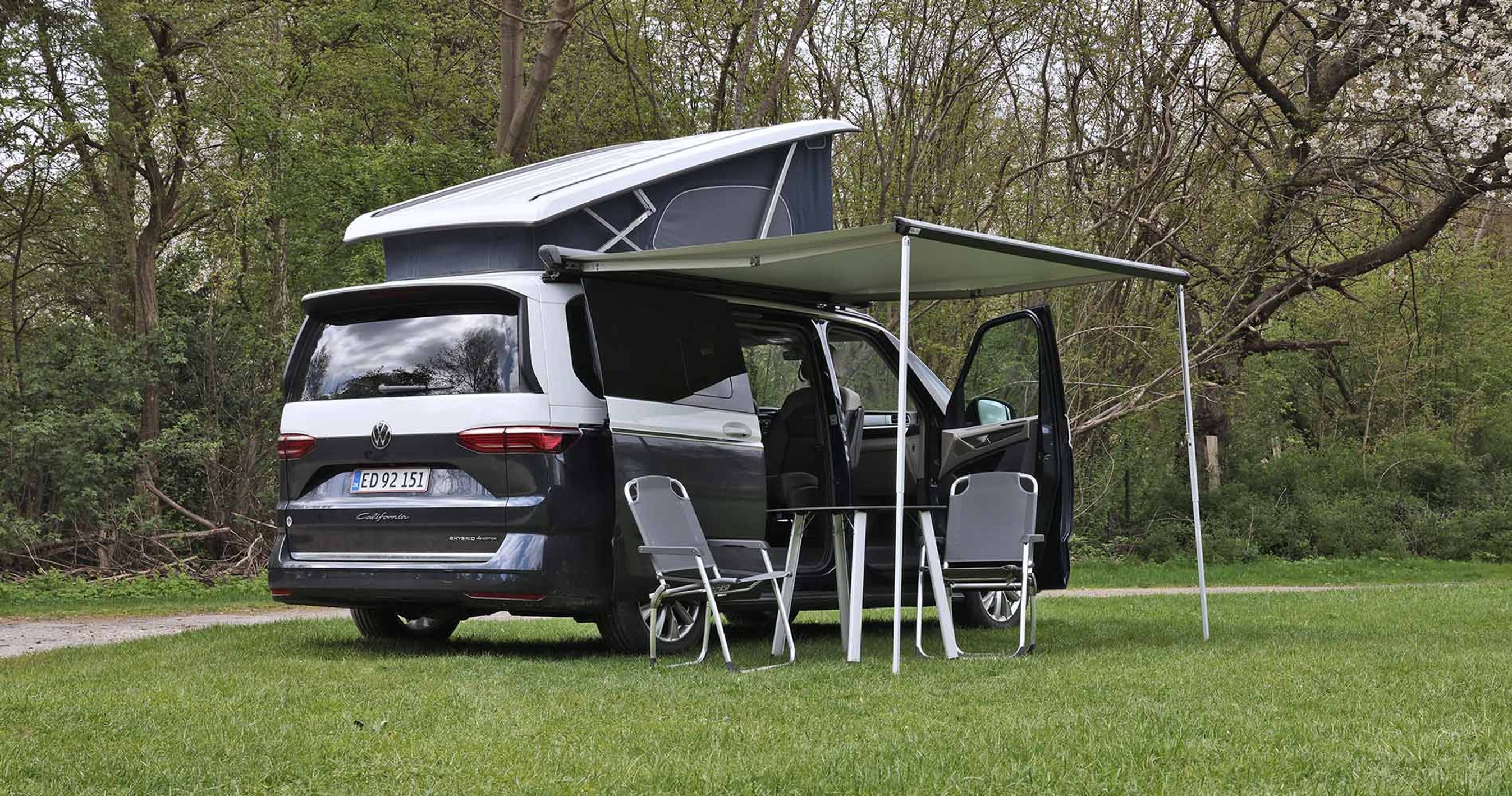VW California med opslået tag og udslået markise holder på græsplæne