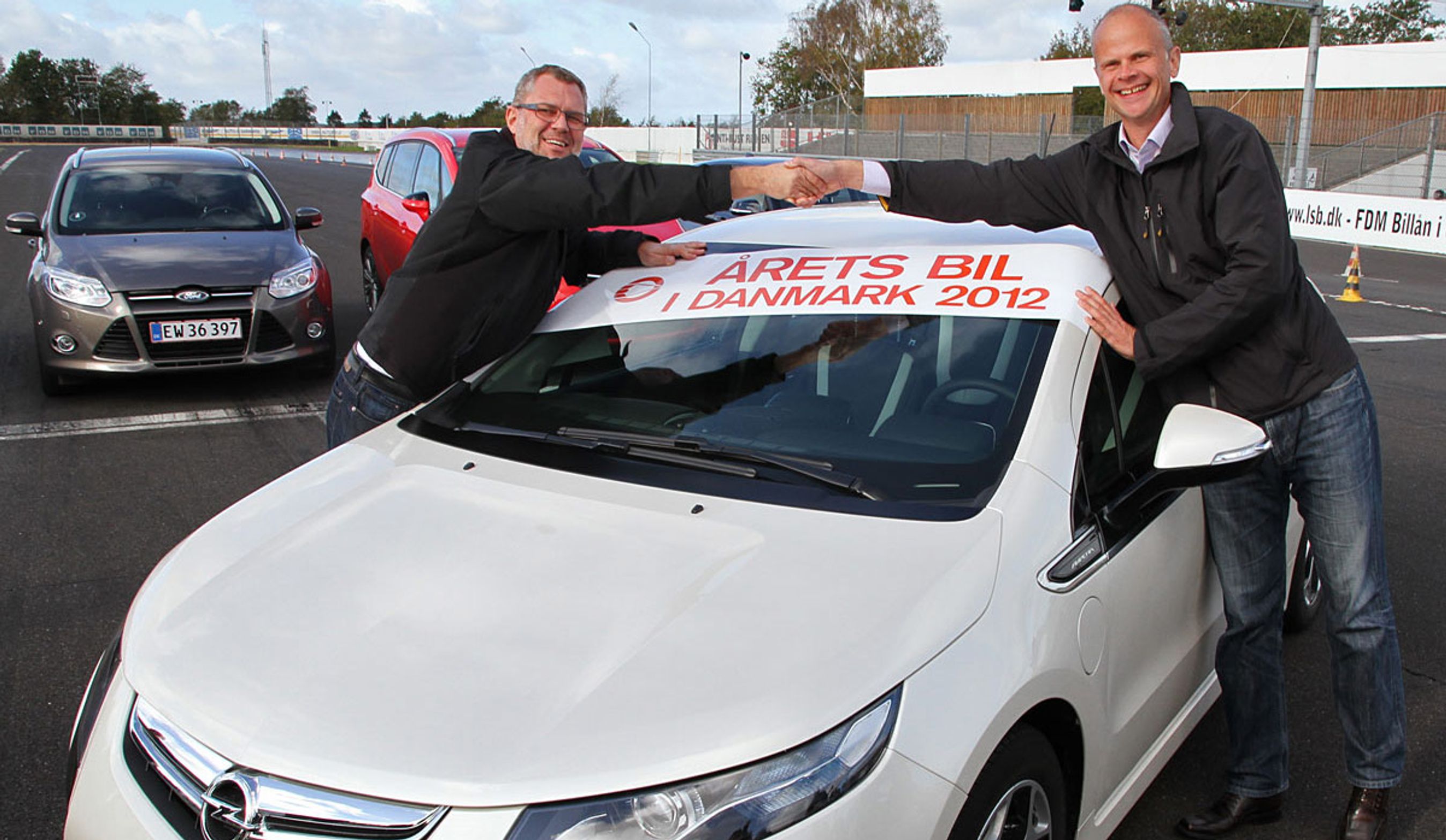 Formanden for Motorjournalisternes Klub Danmark, Mikkel Thomsager (t.v.), lykønsker Opels informationschef, Erik Morsing, med Amperas sejr.
