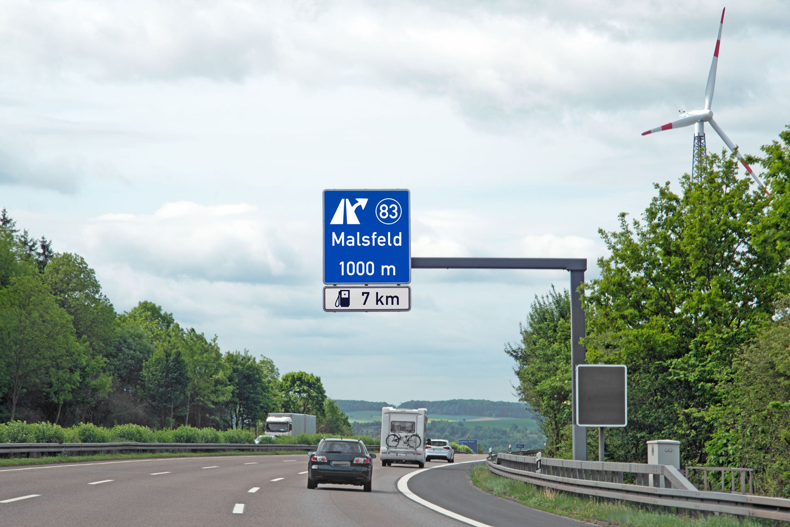 Bil på motorvej med skilt til tankstation