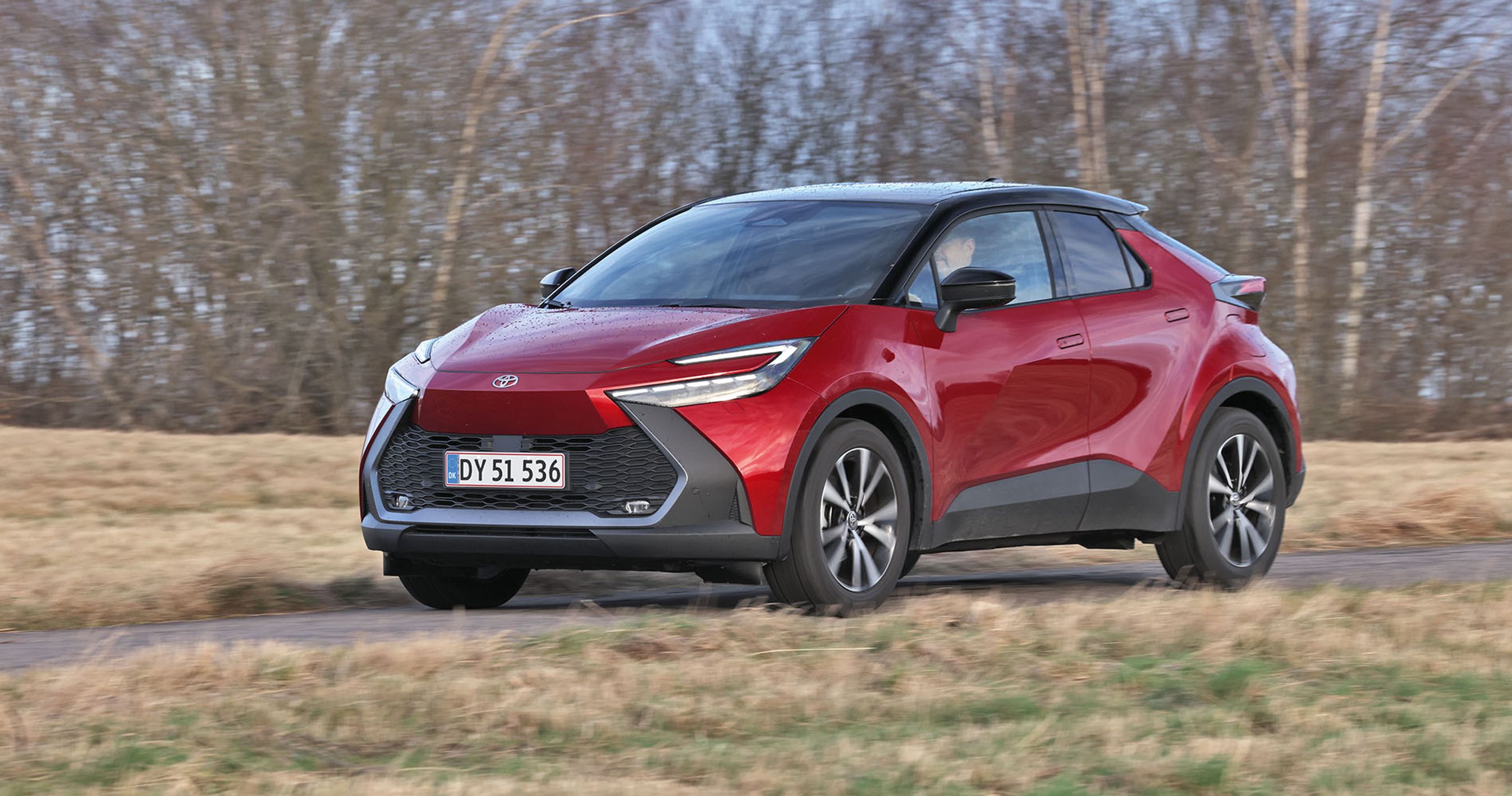 En rød Toyota C-HR kører på landevej med træer i baggrunden