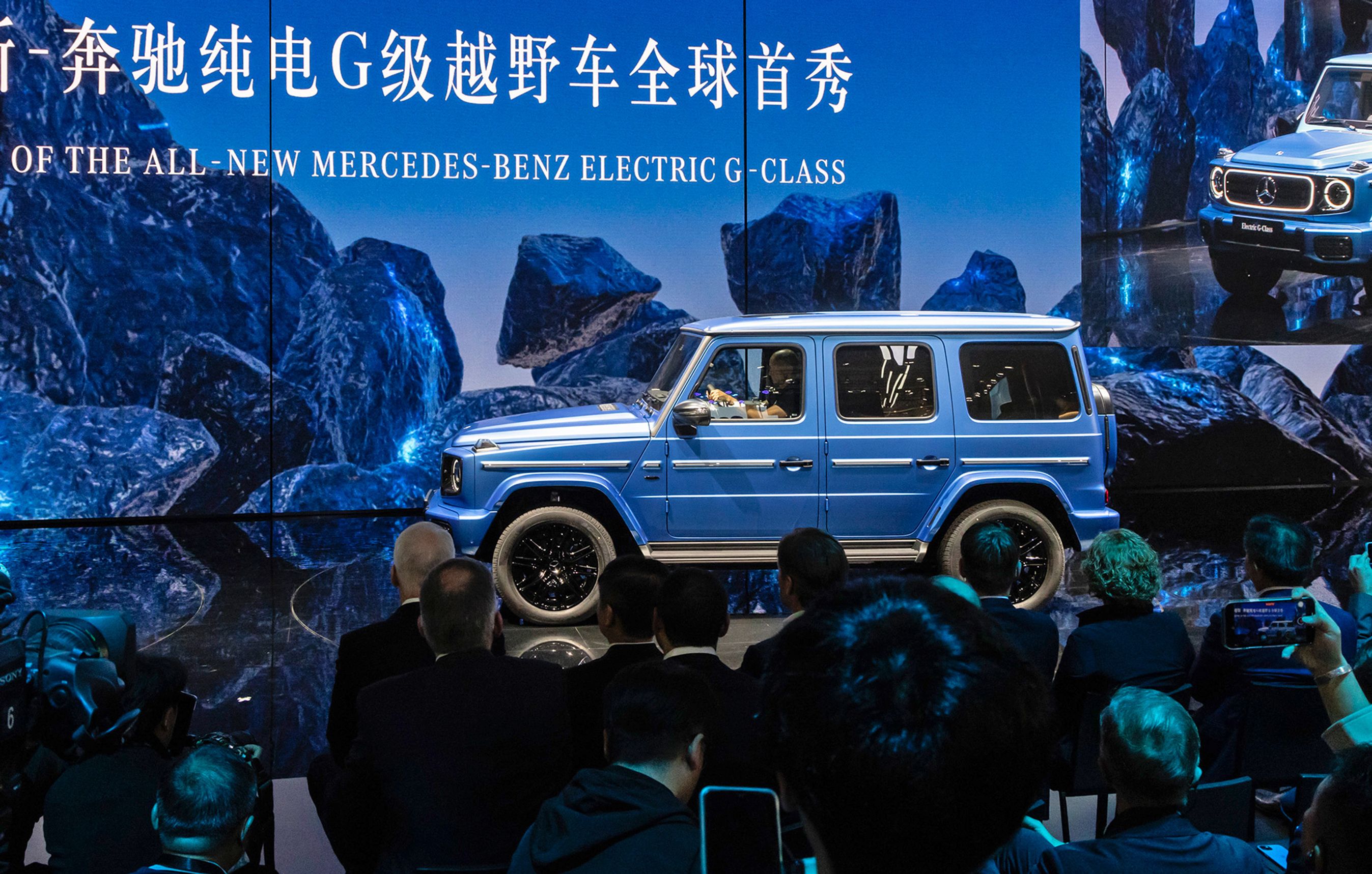 Blå Mercedes G-klasse med tilskuere i forgrunden.