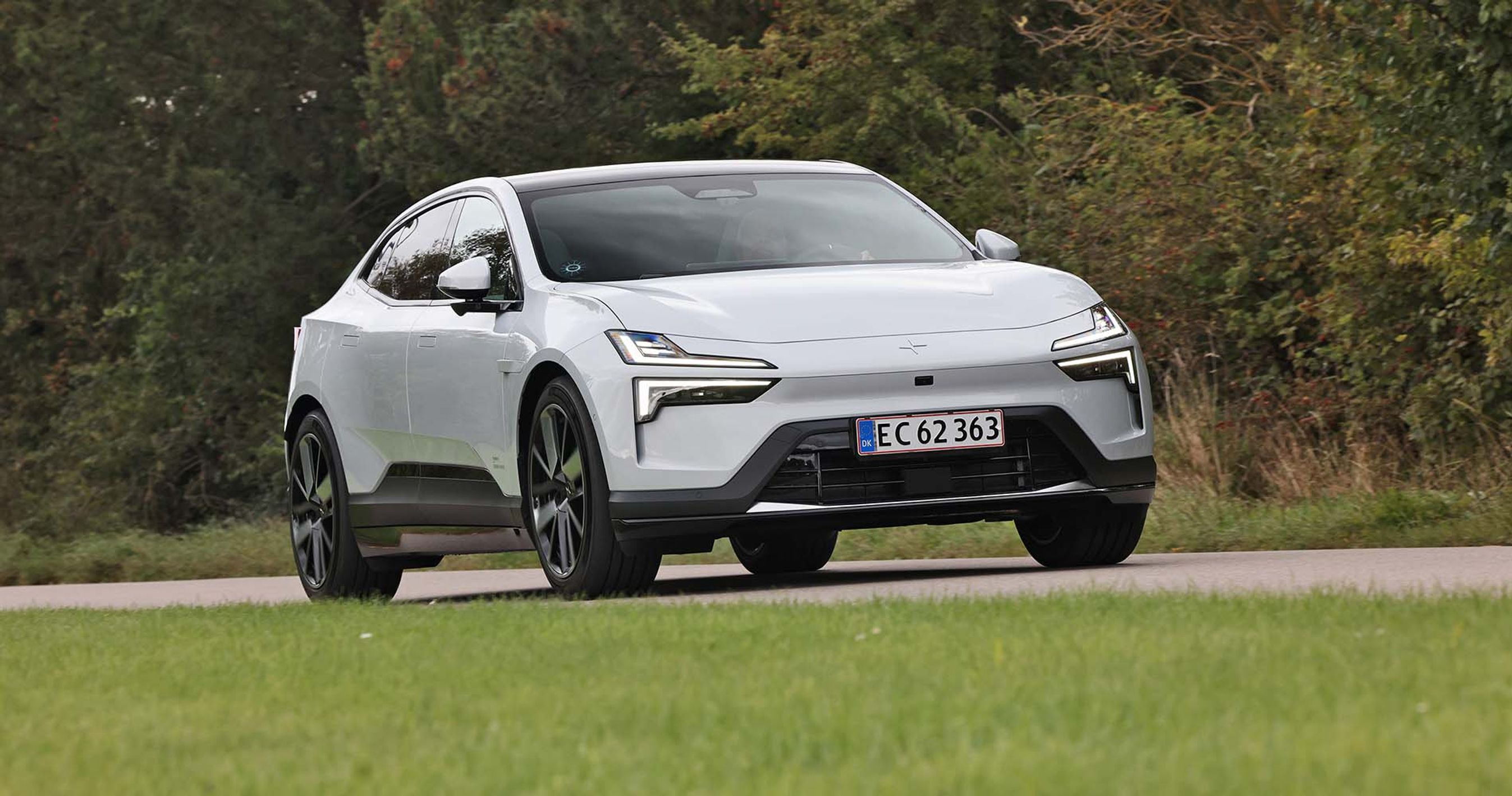 En Polestar 4 set forfra kører på en vej med træer i baggrunden.