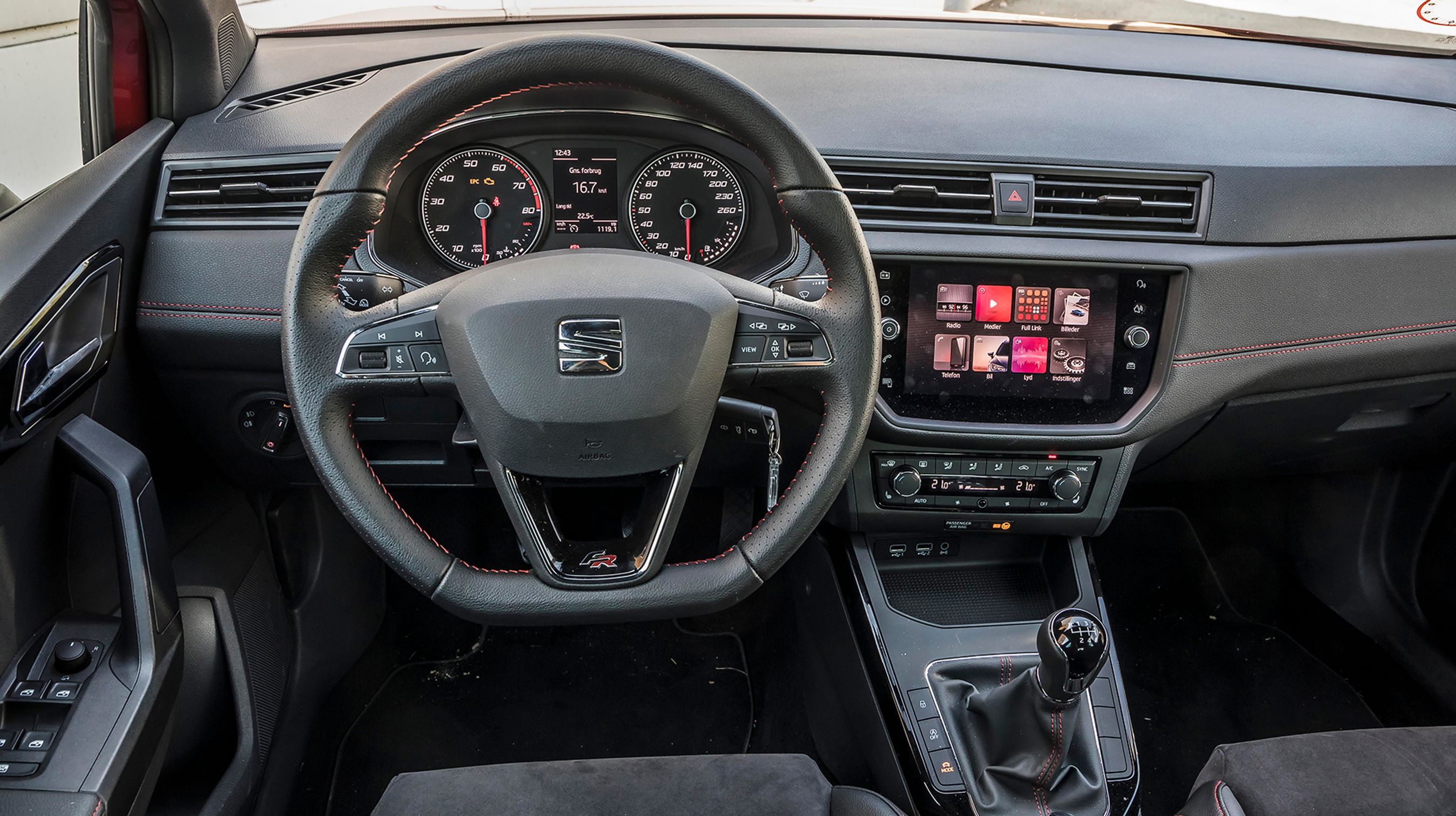 Stor omdrejningstæller og et lækkert læderrat med røde syninger løfter en ellers trist kabine med billig hård plast. Der er god fralægningsplads omkring føreren – et klart plus ved Arona.