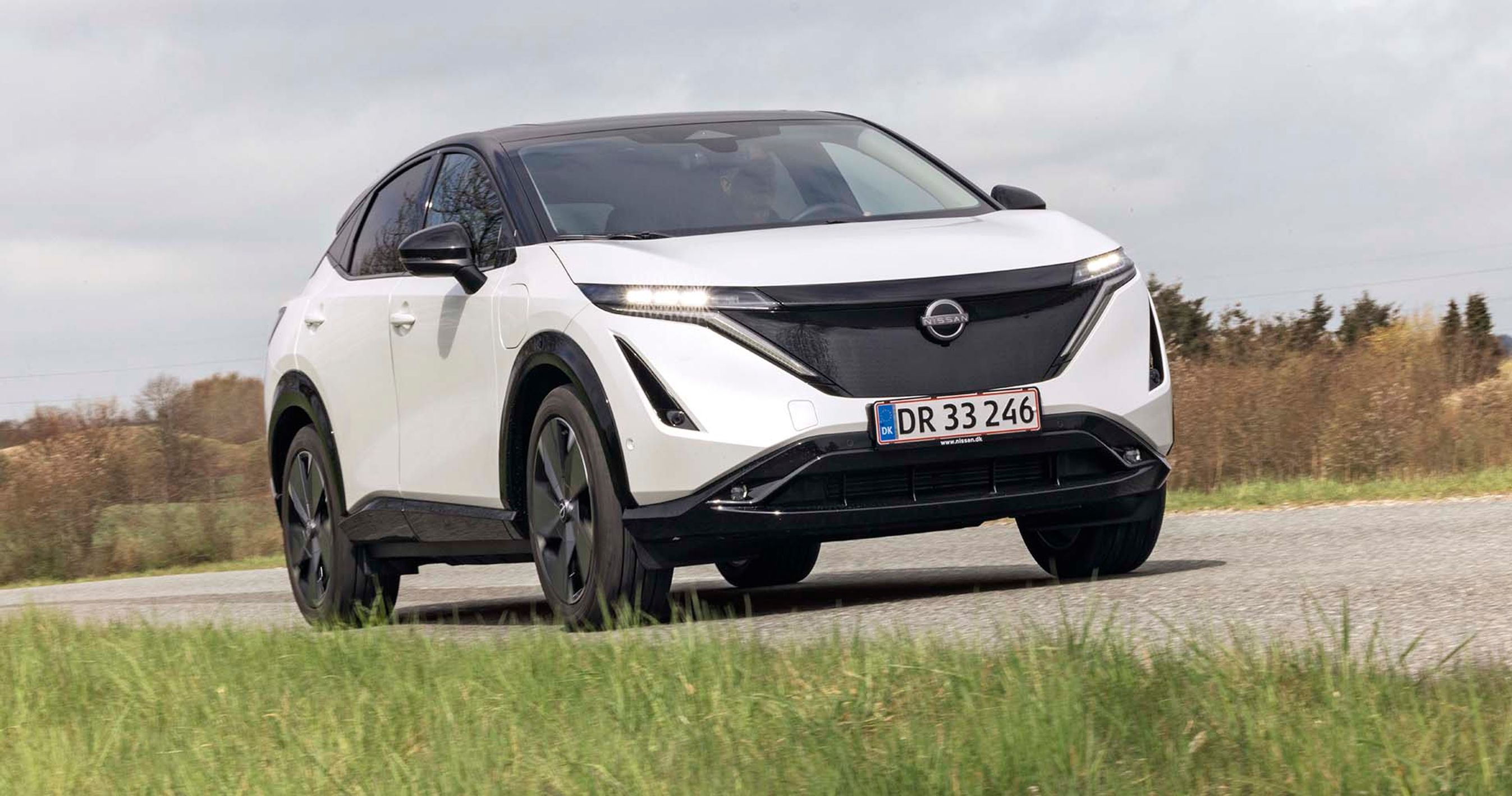 En hvid Nissan Ariya elbil kører på en landevej.