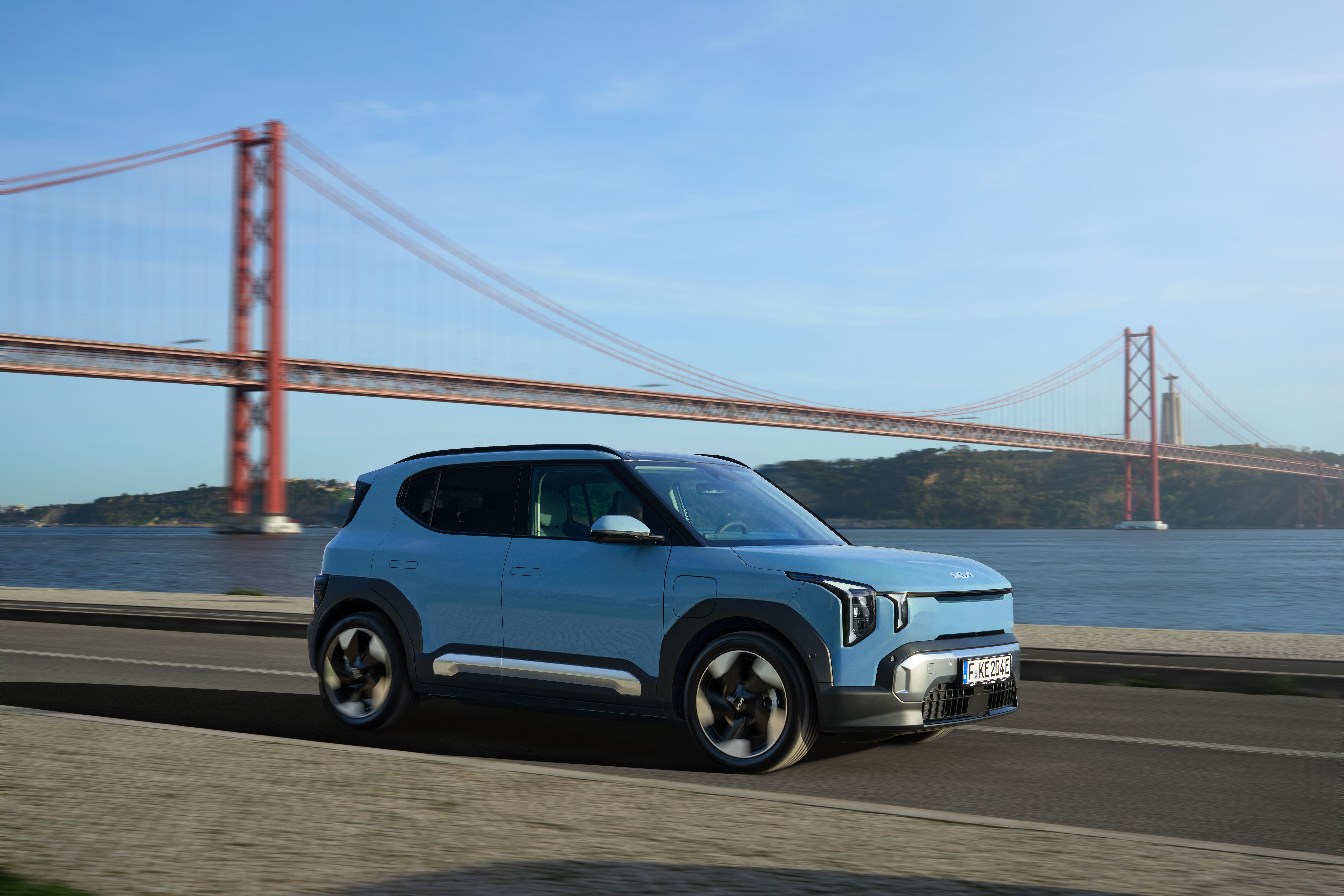 Kia EV2 kører på vej med rød bro i baggrunden