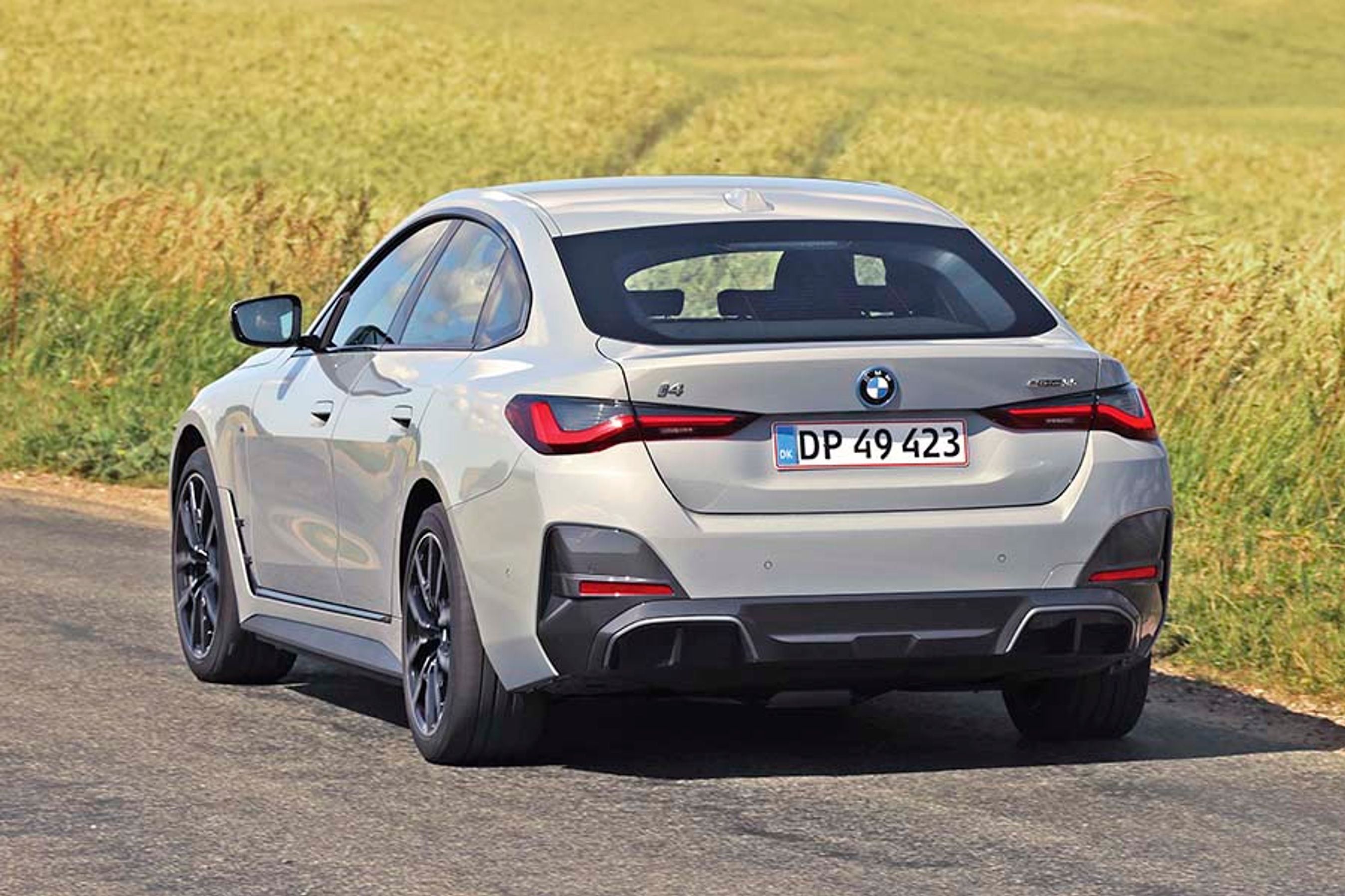 BMW i4 set bagfra, mens den kører på landevej med græs i baggrunden