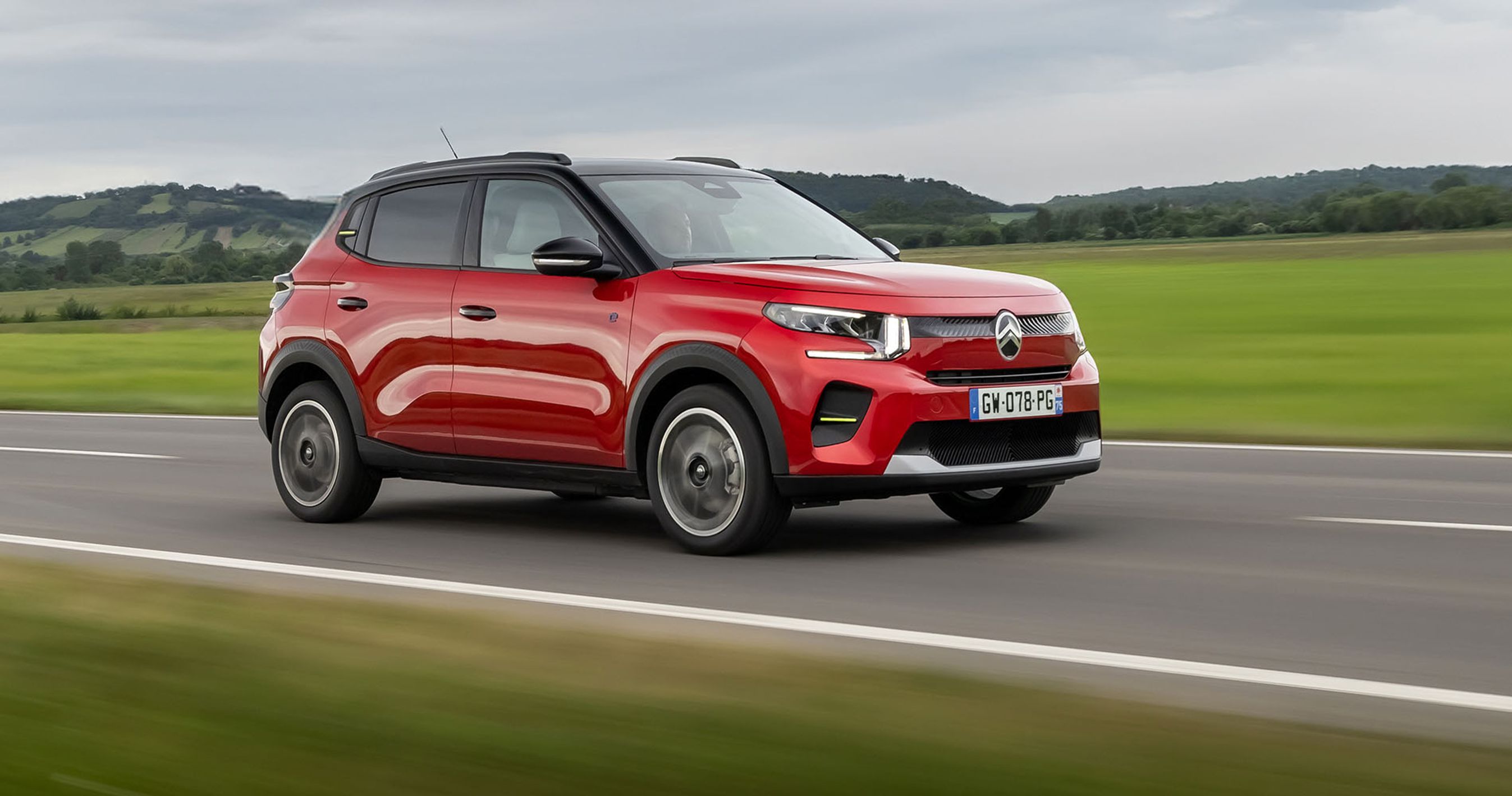 En rød Citroën ë-C3 kører på en vej med græs i baggrunden