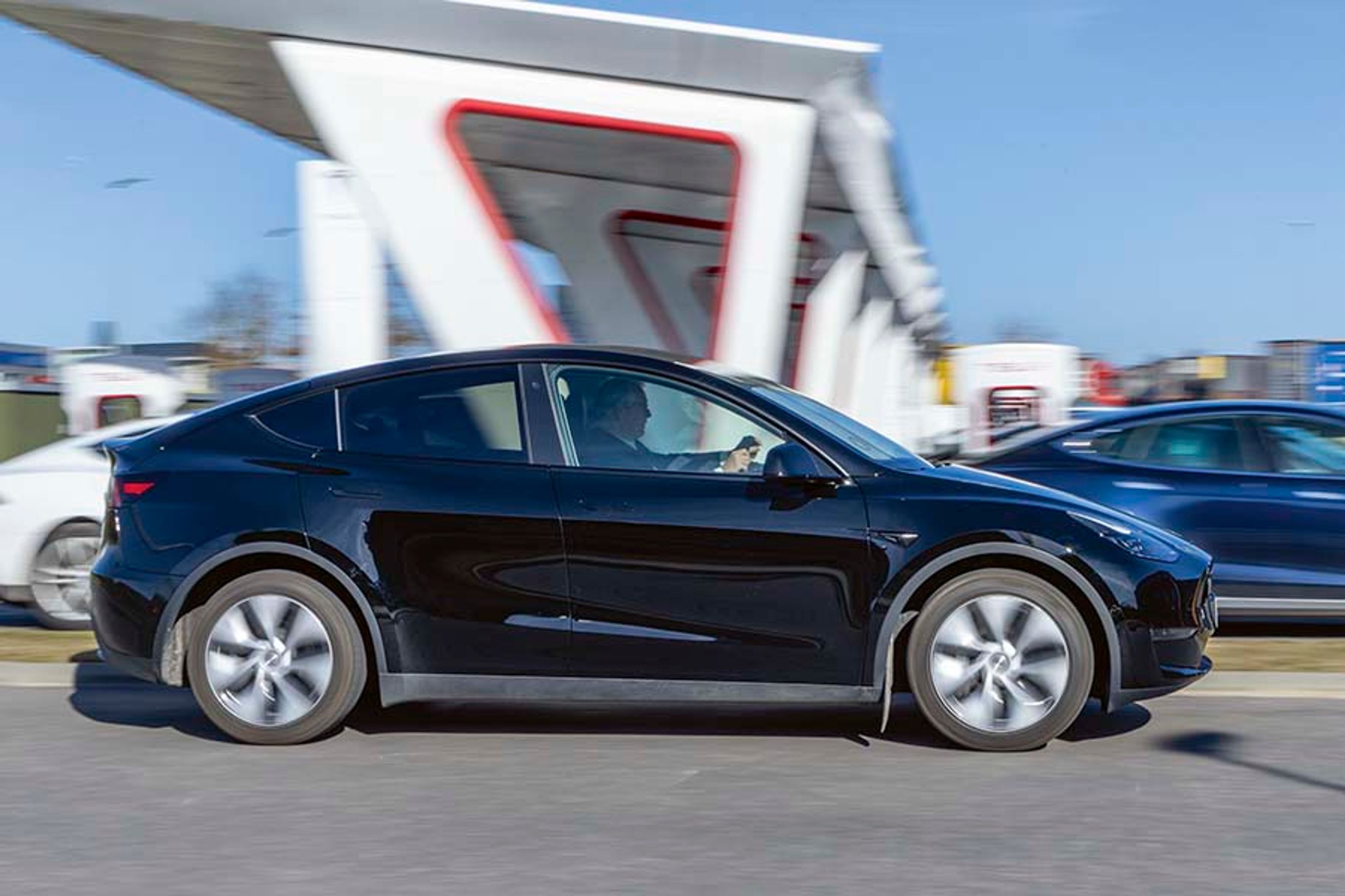 Sort Tesla Model Y kører forbi en lynladestation