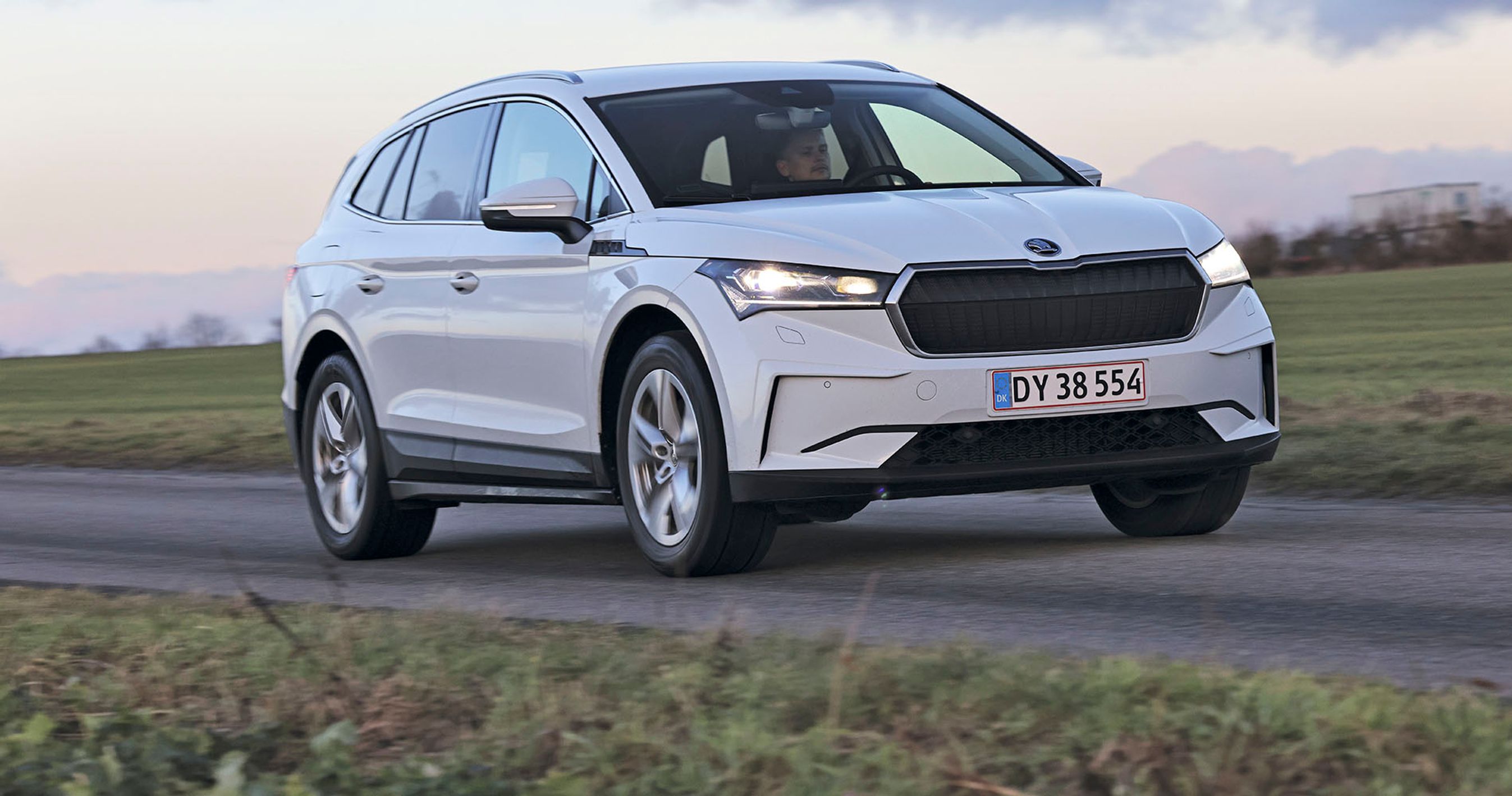 En Skoda Enyaq elbil set forfra kører i tusmørke på en landevej