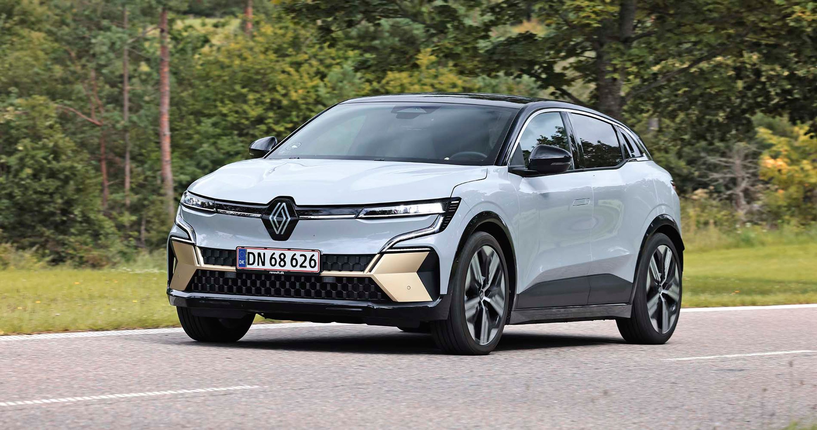 Elbilen Renault Megane E-Tech set skråt forfra, mens den kører på en vej med træer i baggrunden.