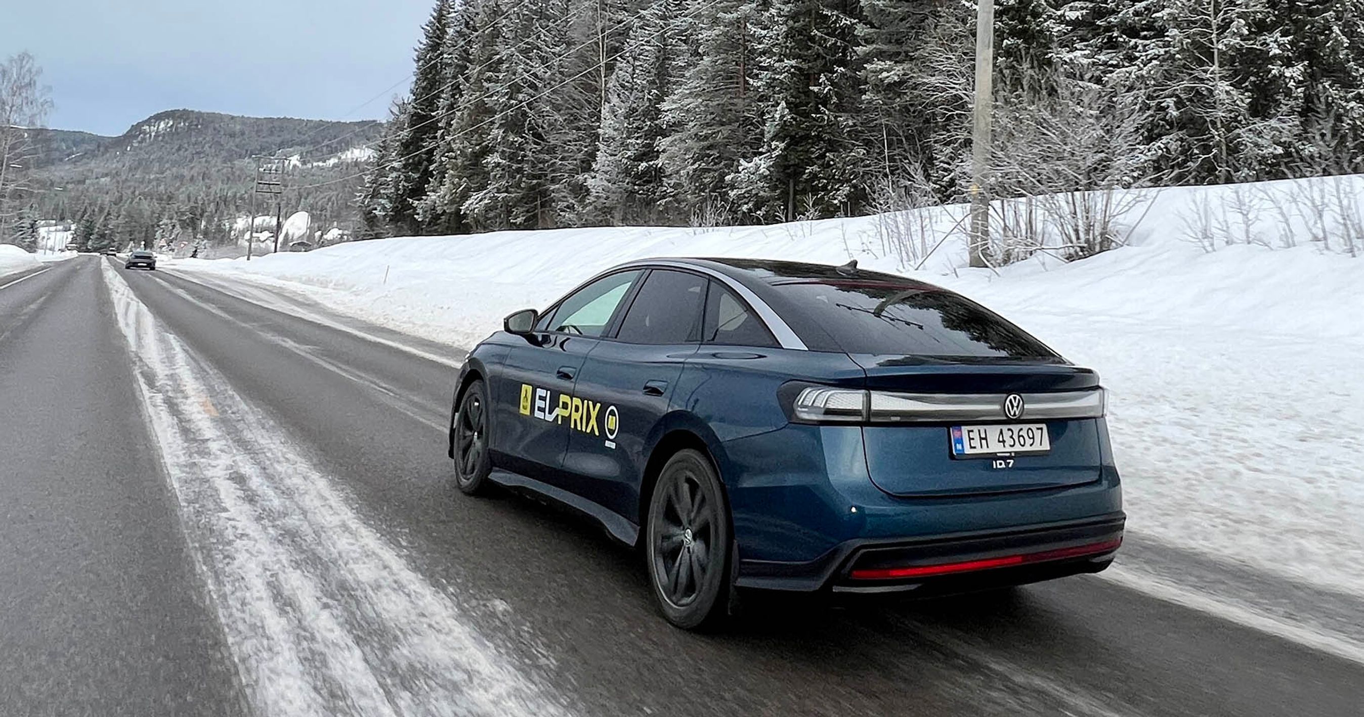 Blå VW ID.7 kører på en norsk landevej med sne i baggrunden.