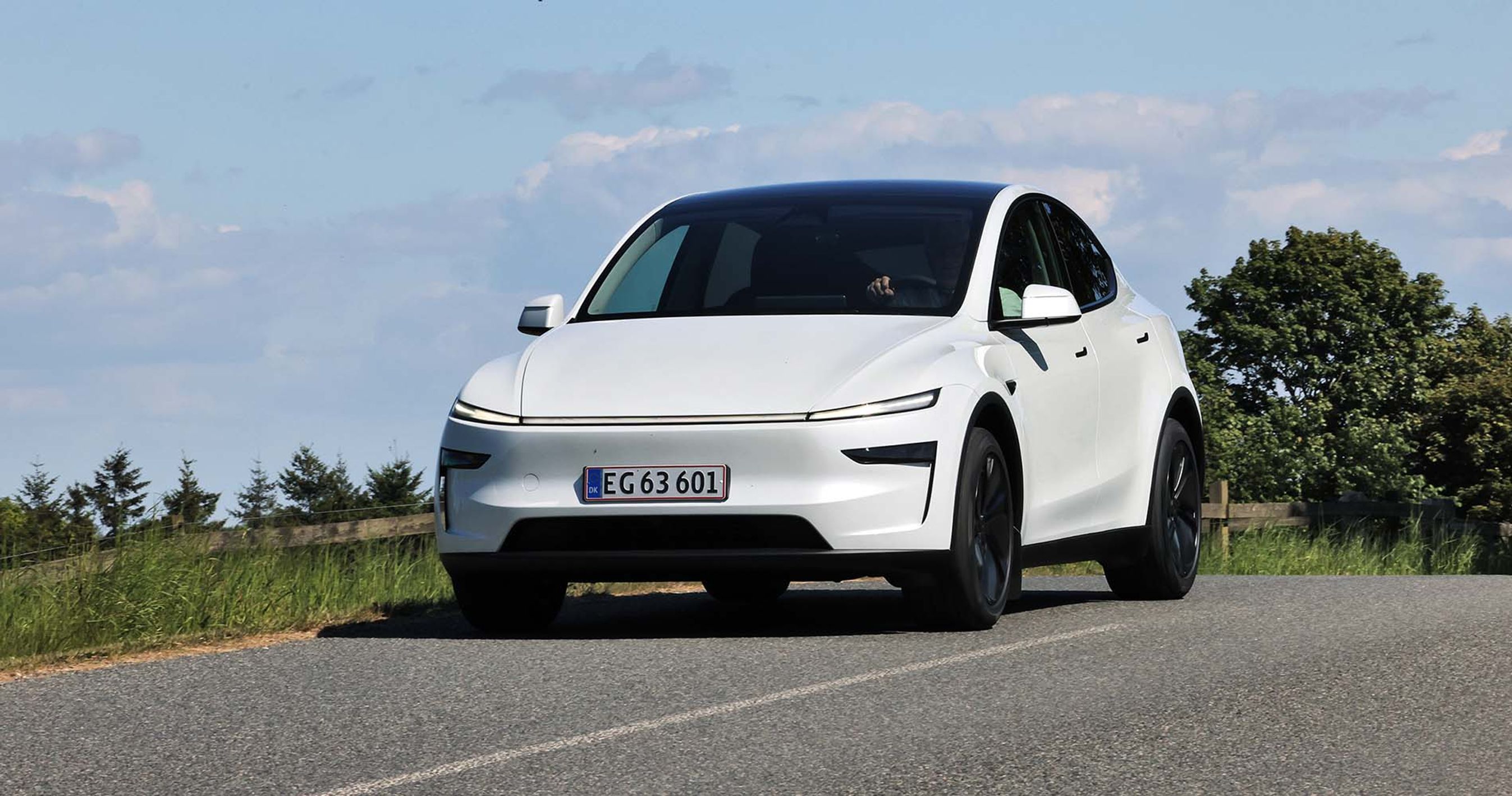 Tesla Model Y kører på en landevej med blå himmel i baggrunden