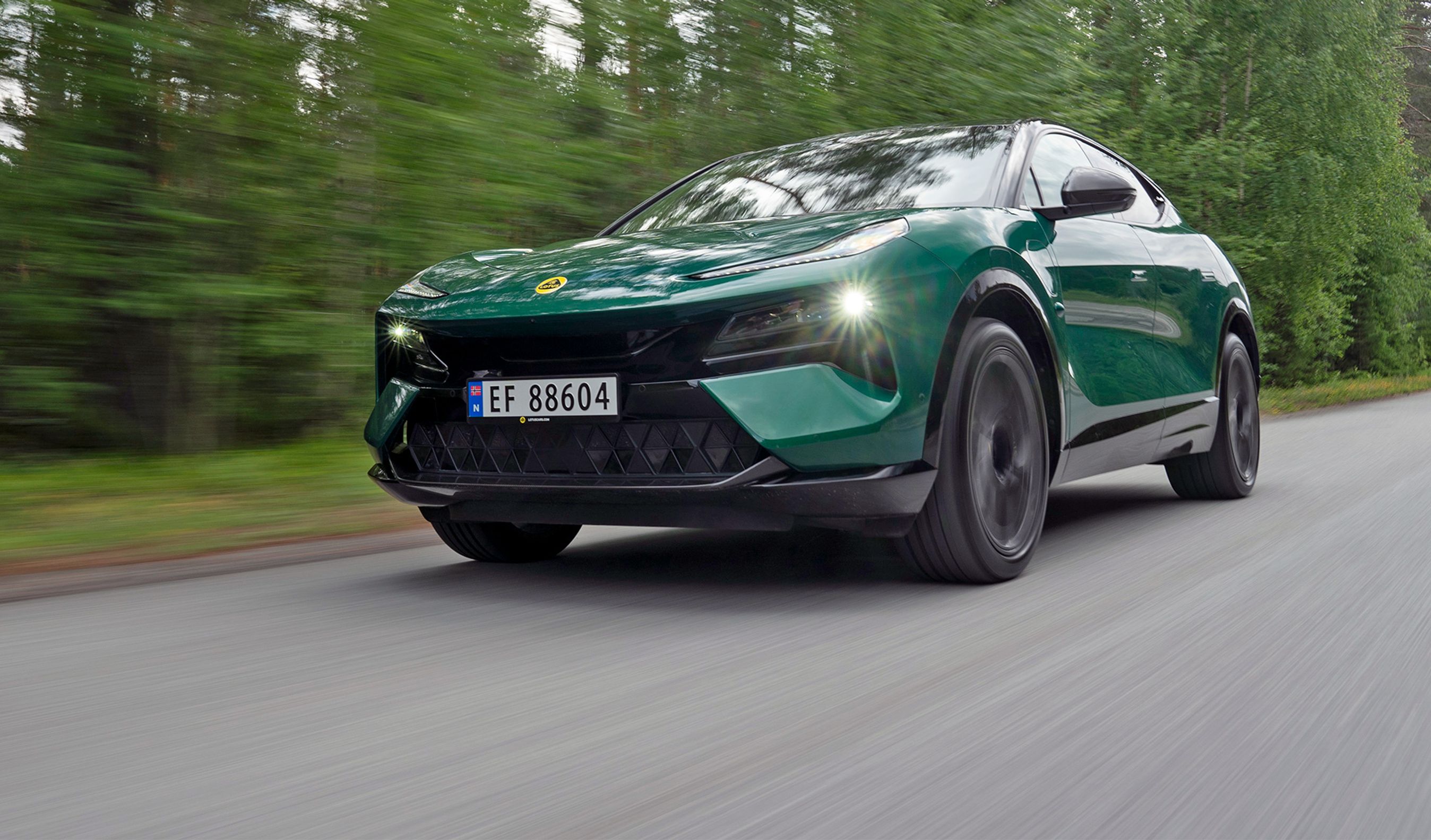 Grøn Lotus Eletre kører hurtigt på vej med skov i baggrunden