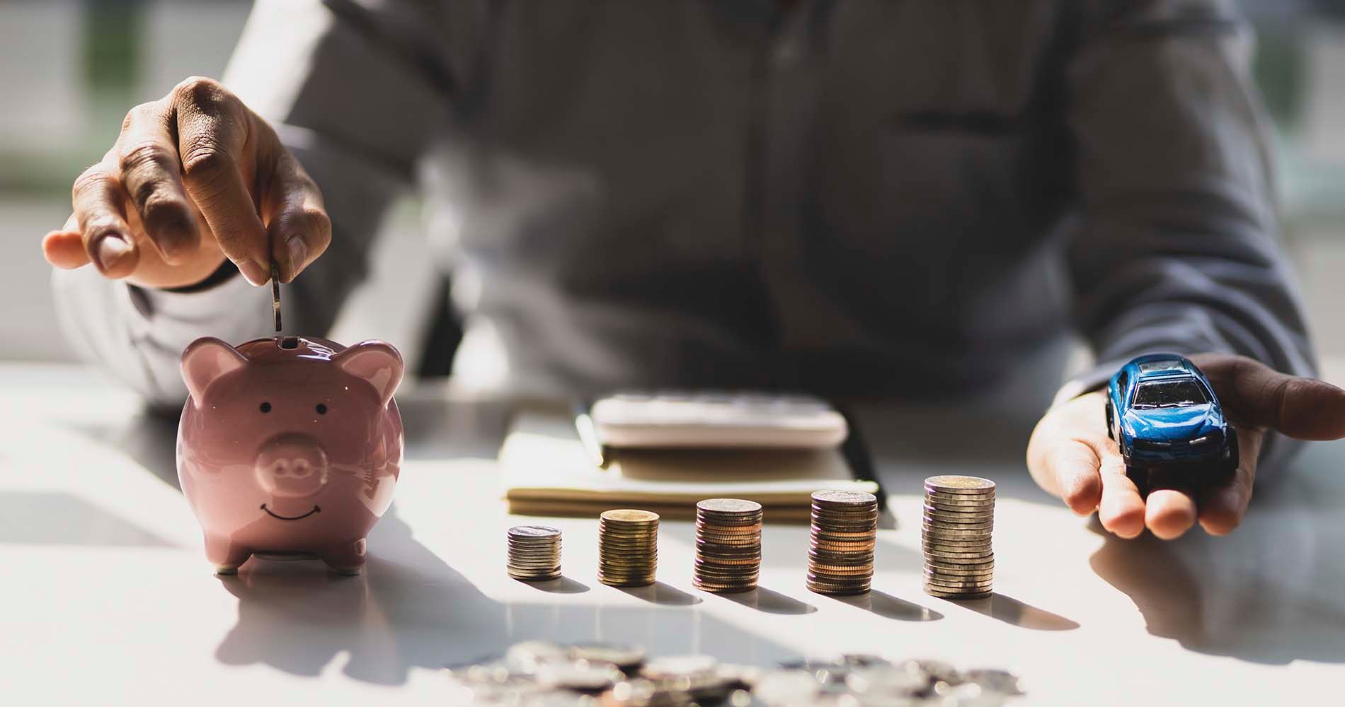 Sparegris, penge og en modelbil på et bord. En mand sidder og betaler for at køre.