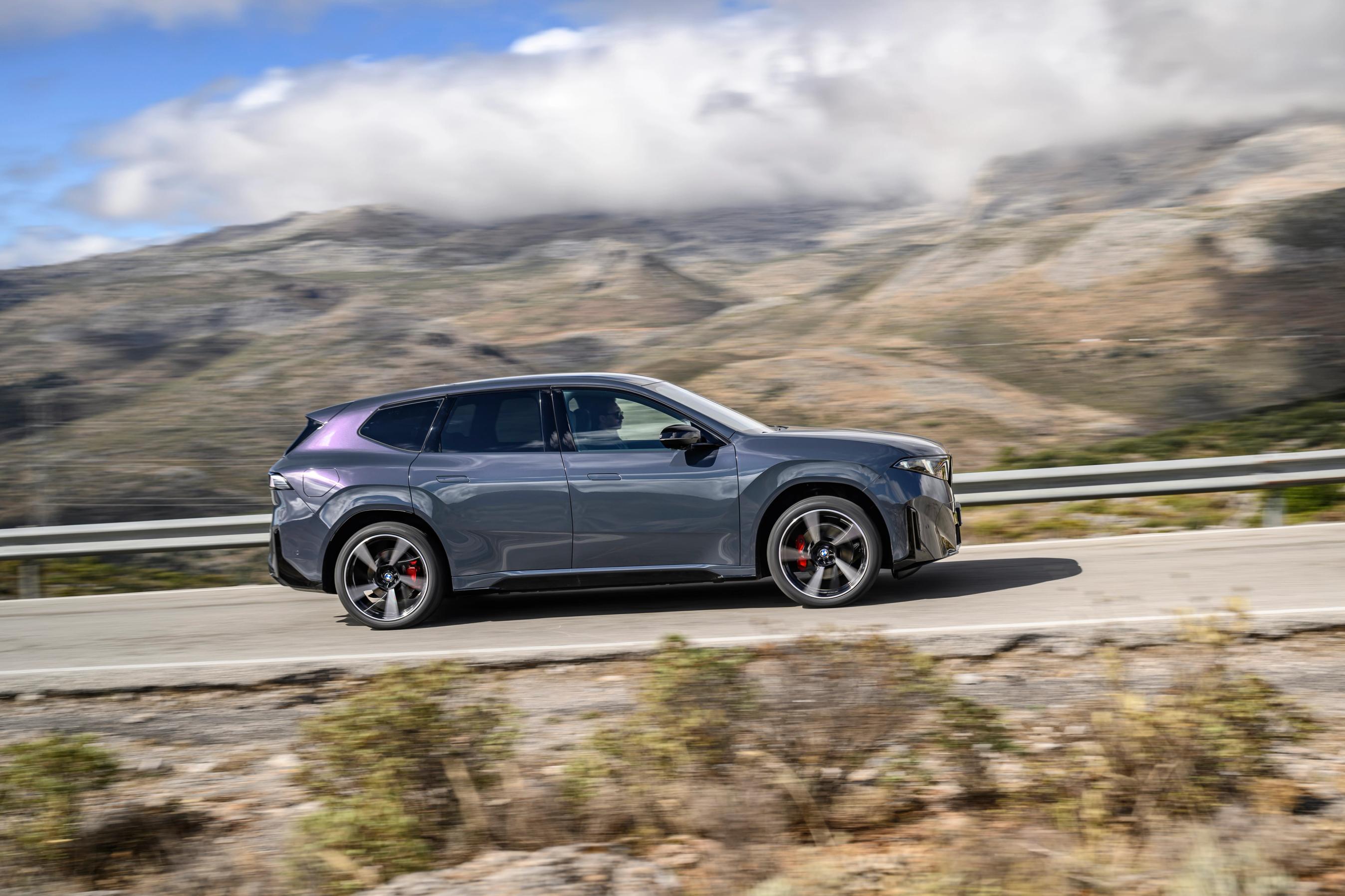 BMW iX3 set fra siden, mens den kører på en bjergvej med skyer i baggrunden