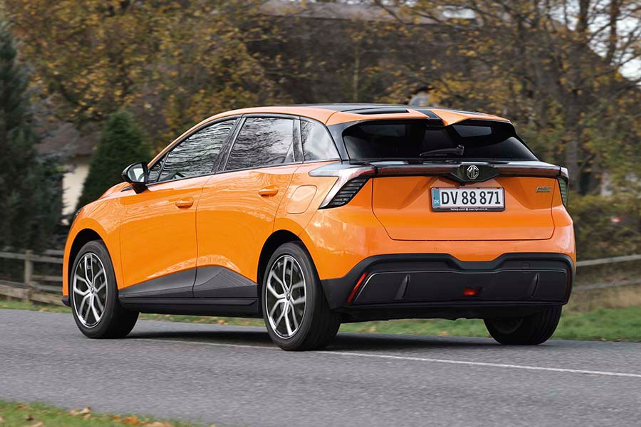 Orange MG 4 set bagfra, mens den kører med træer i baggrunden