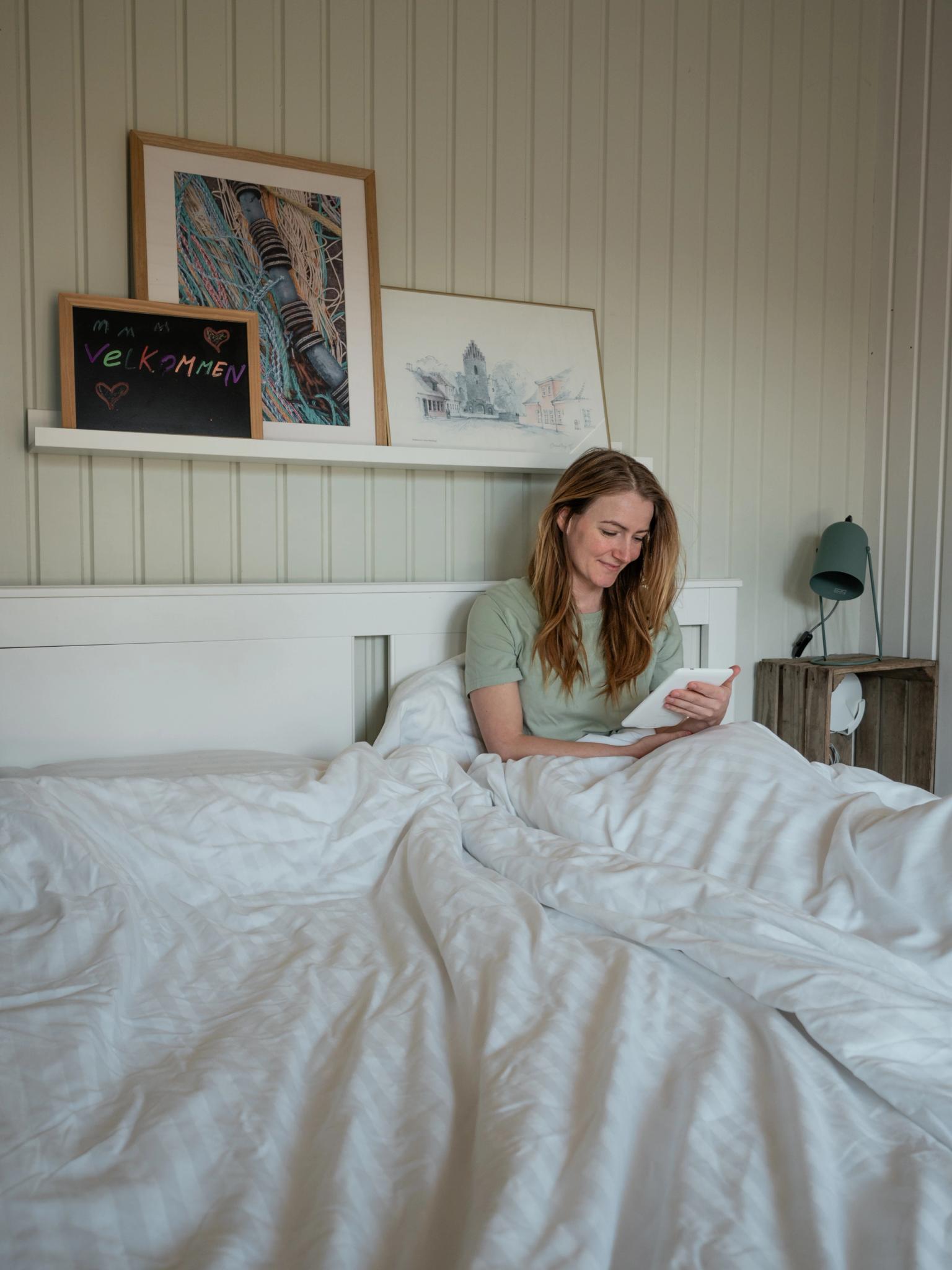 Kvinde sidder i en dejlig seng hos Danhostel og nyder en rolig morgen