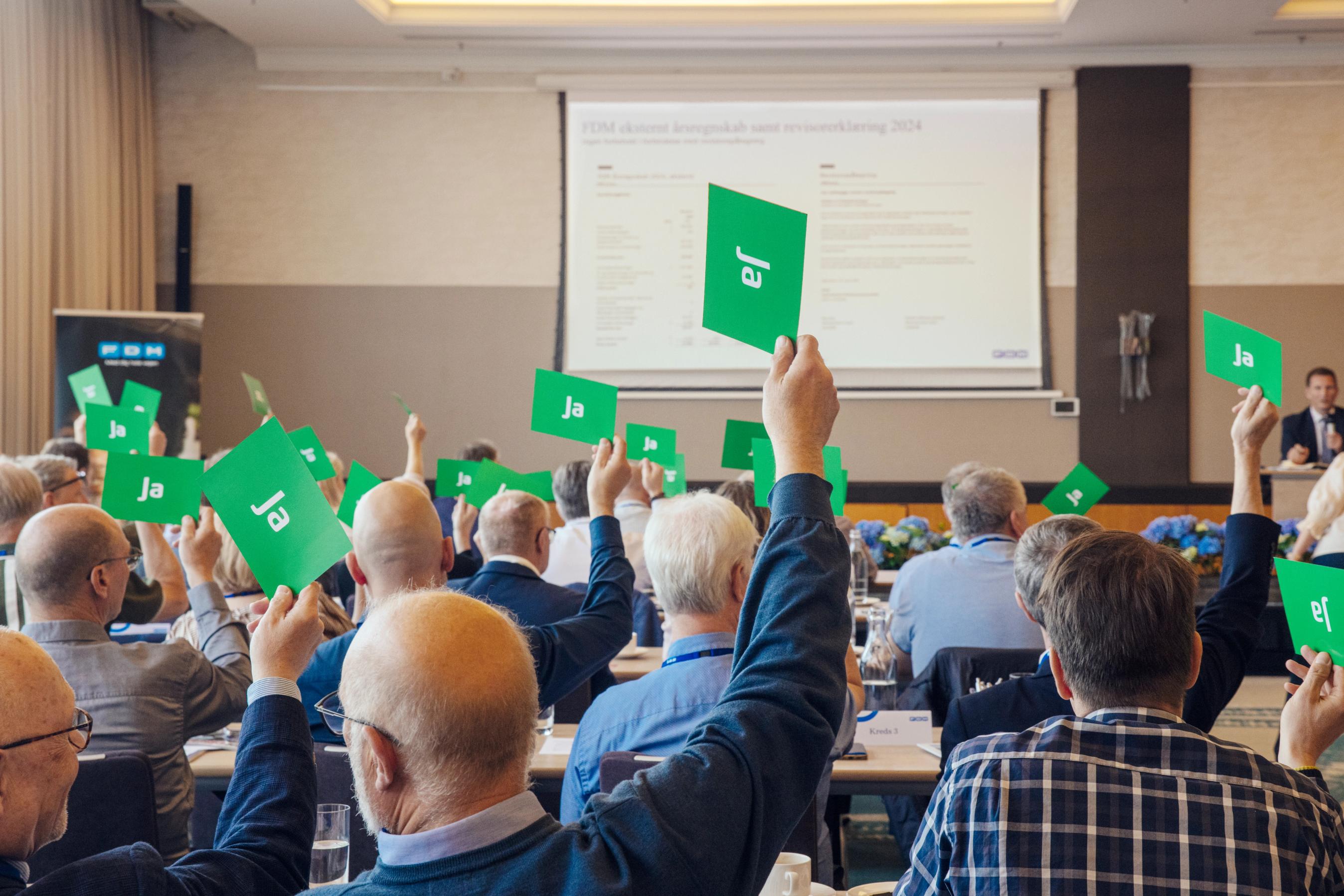 Medlemmer af FDMs repræsentantskab rækker armen i vejret og afgiver stemme til valg