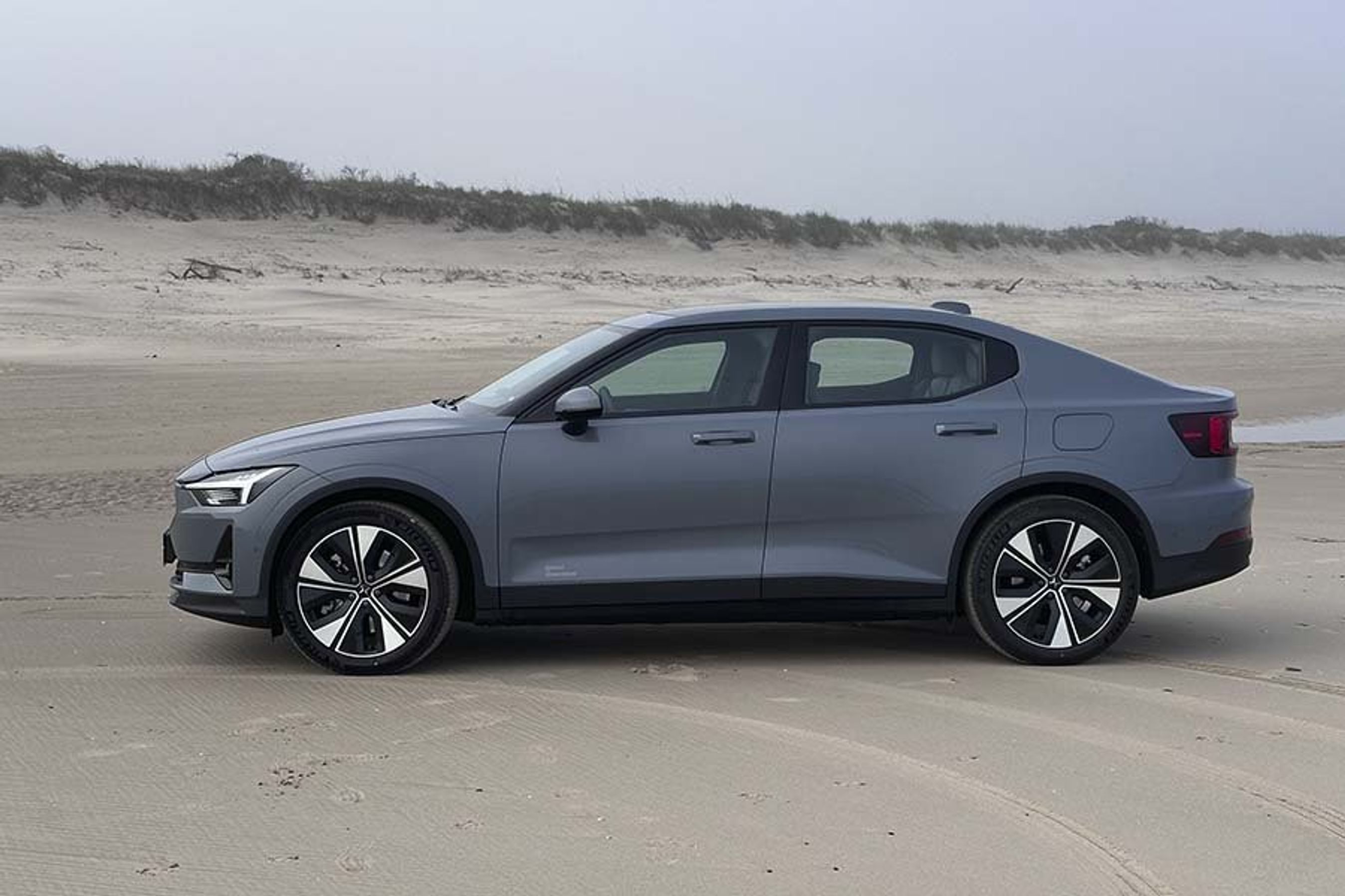 Polestar 2 set fra siden, mens den holder på en strand med klitter i baggrunden