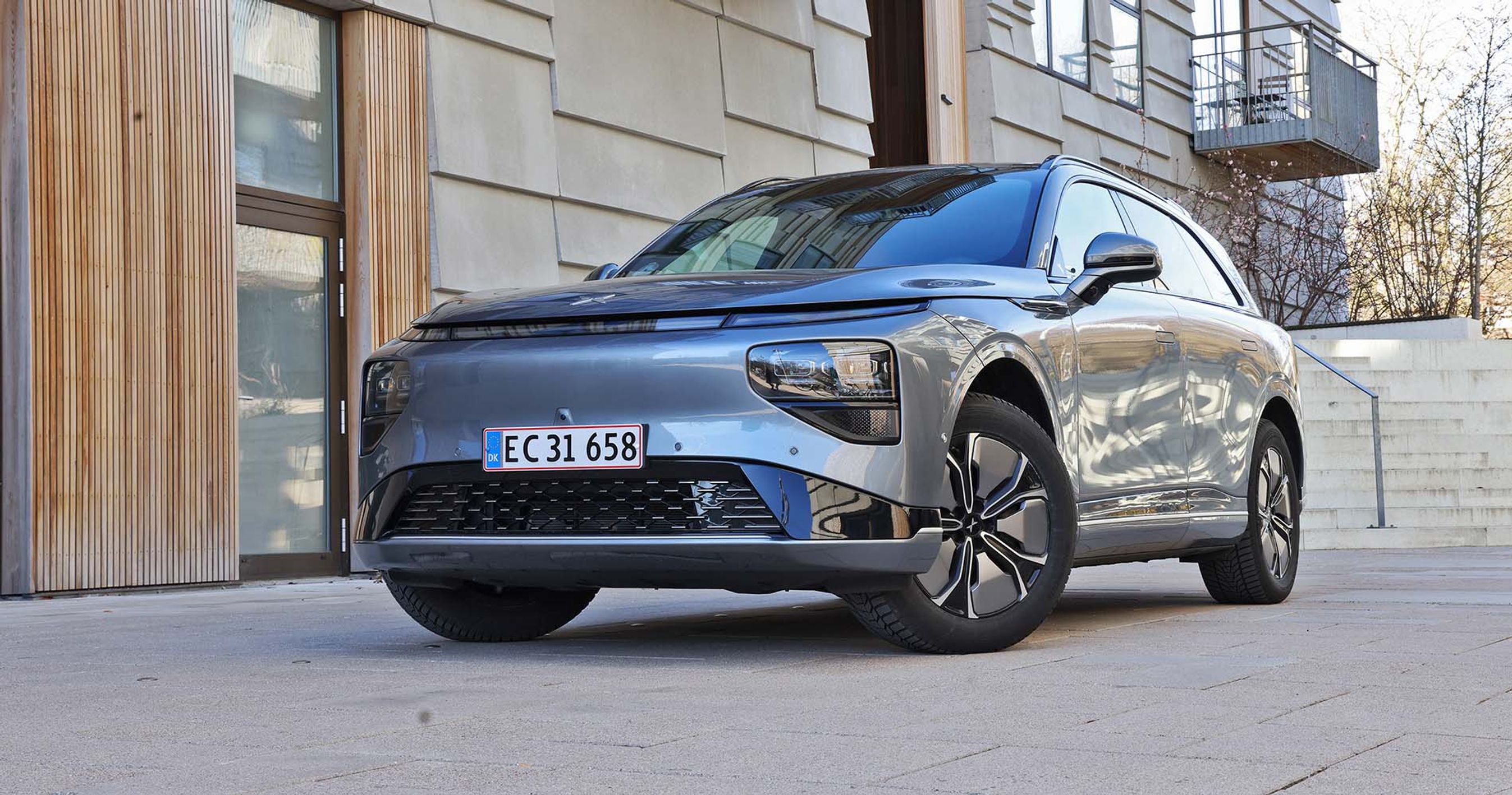 Xpeng G9 parkeret foran bygning med træpaneler på facaden