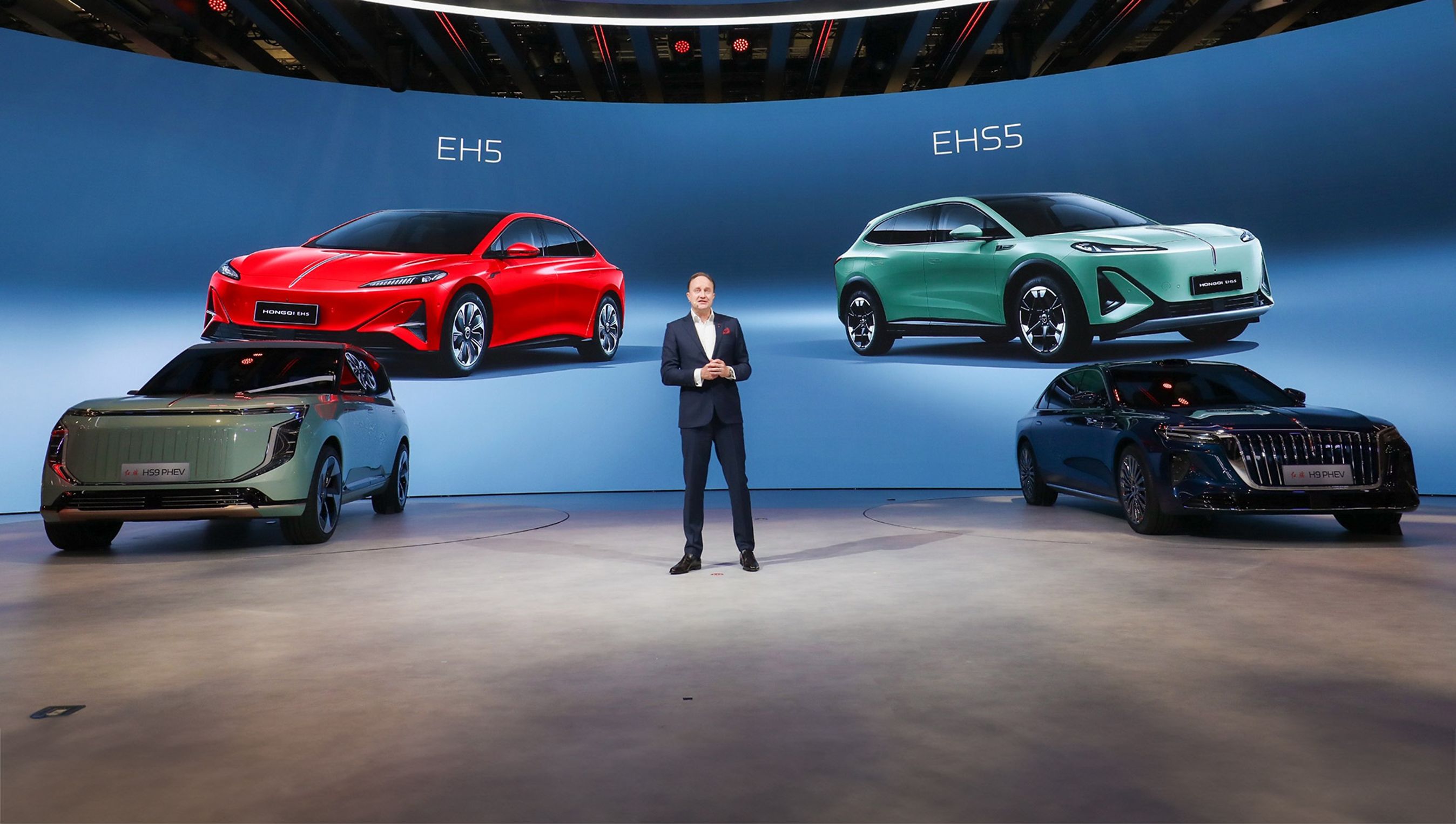 Mand på scene omgivet af fire biler.