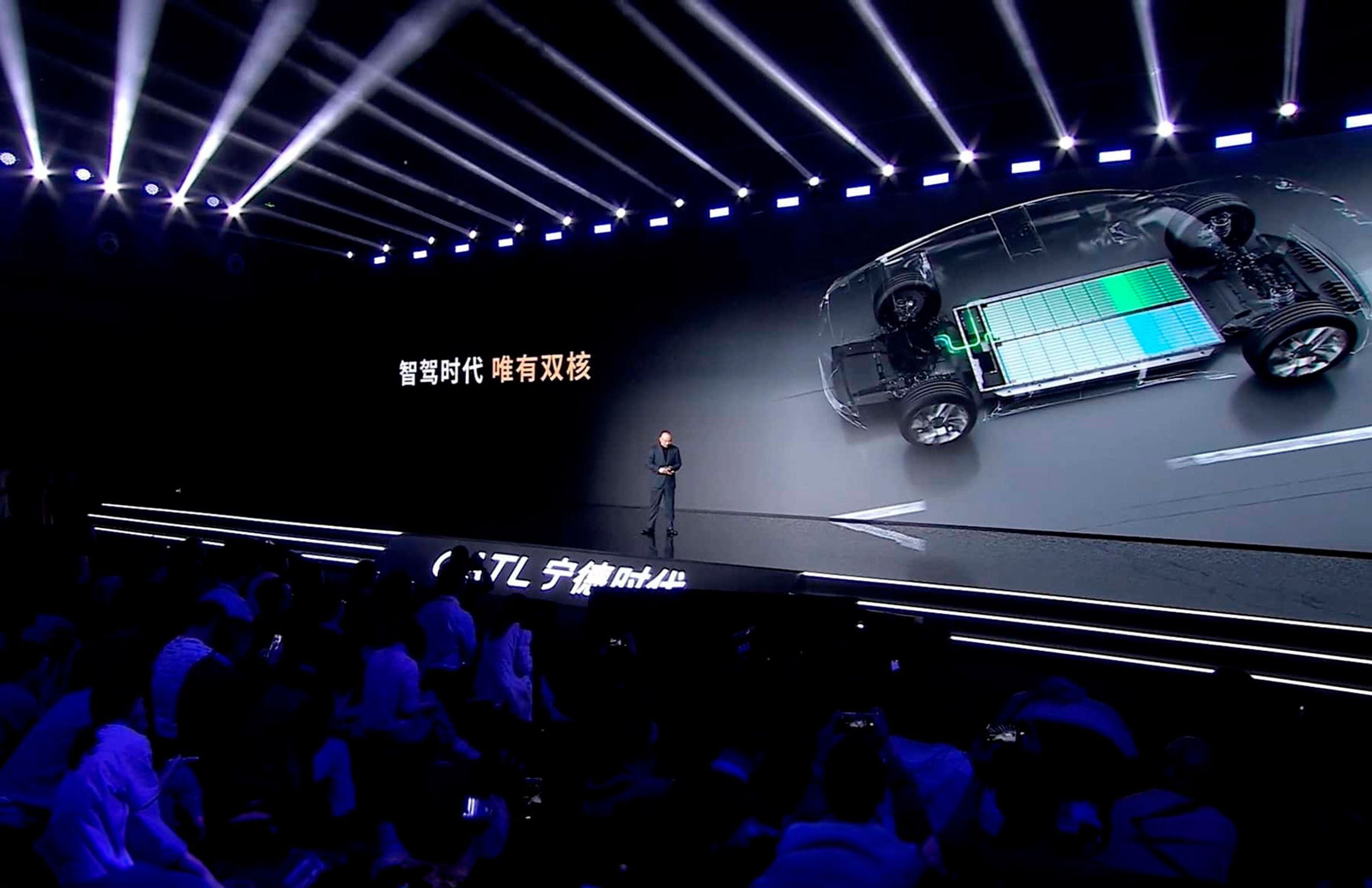 Mand på scene med publikum i forgrunden og billede af batteri på skærm.